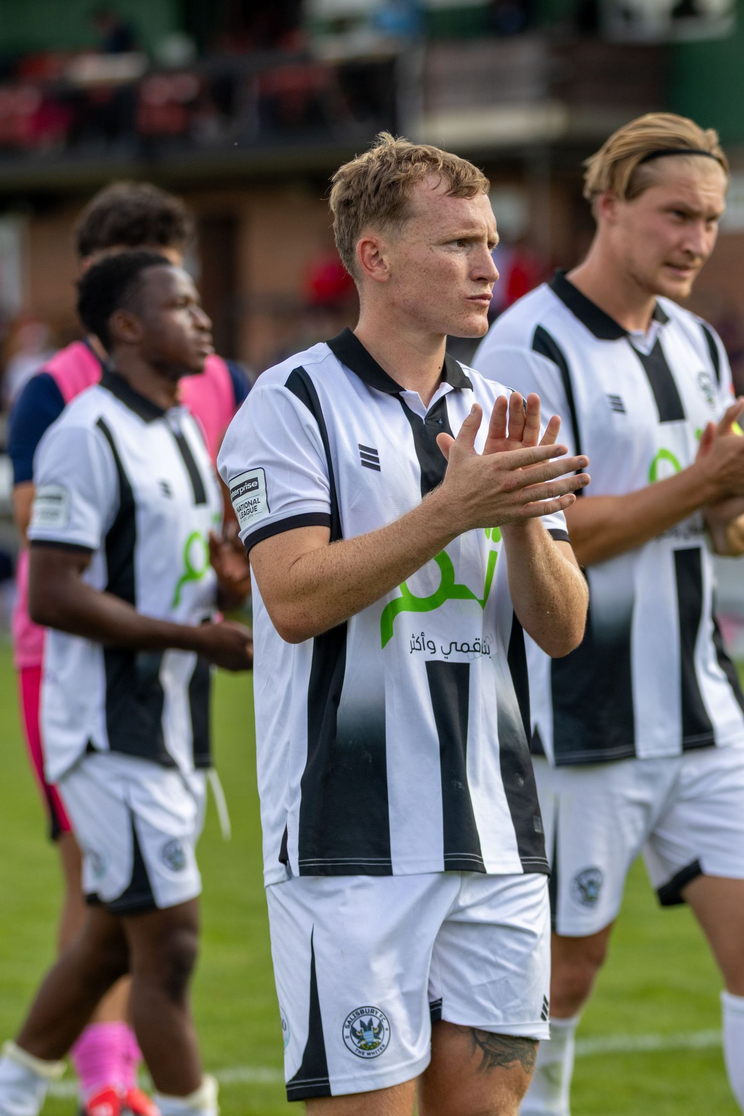 football players in black and white striped jerseys walk on field, with centre player clapping hands after a match.