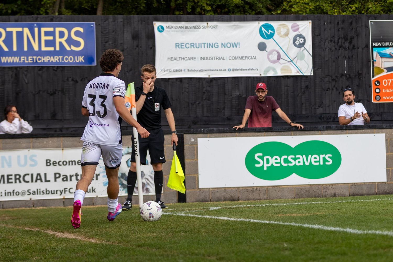 Football match action with player number 33 dribbling near the touchline, referee and linesman watching closely.