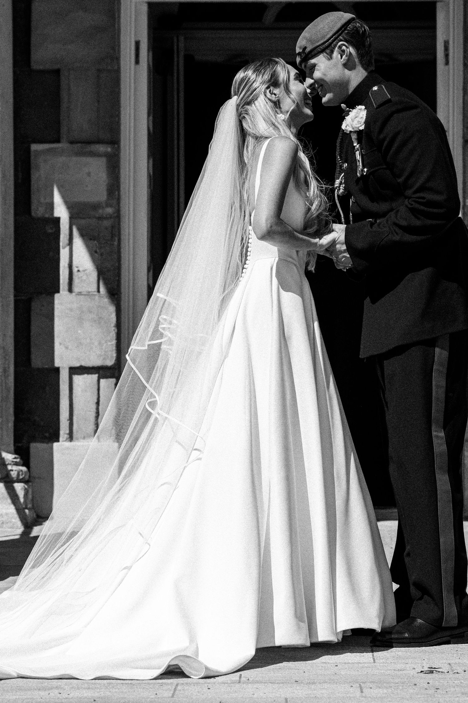 Black and white photo of bride in white gown and groom in military uniform sharing a romantic moment.