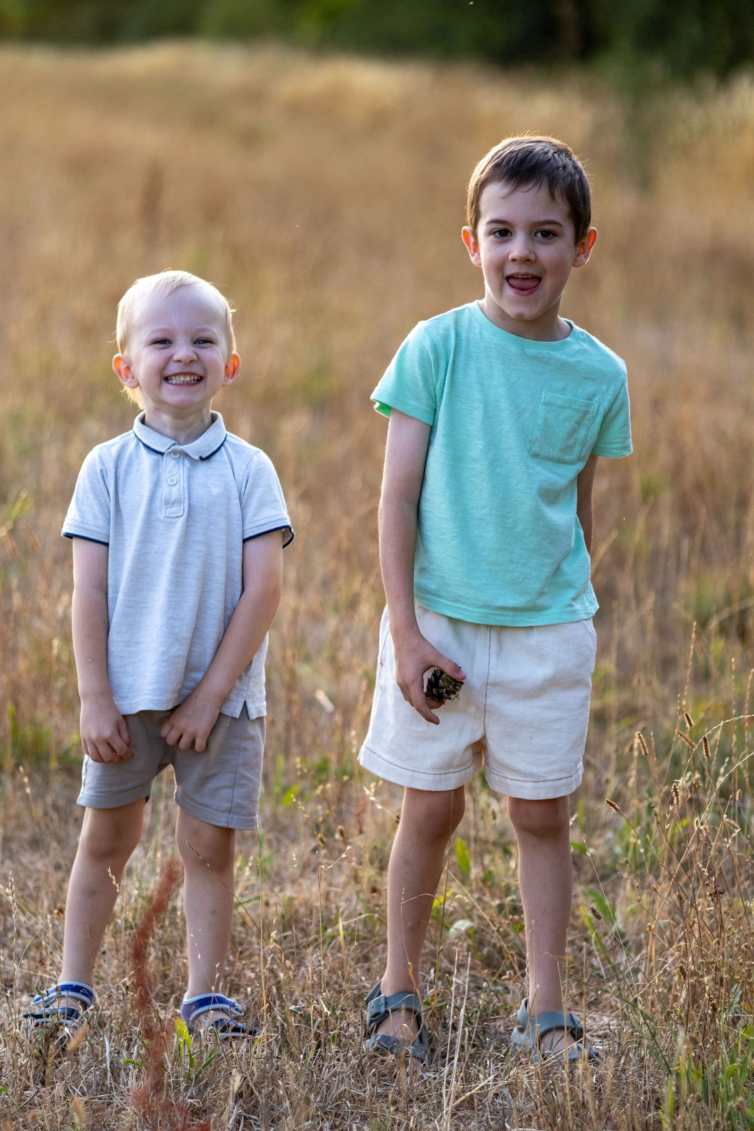 Two young brothers smiling and posing together in a sunny golden field during summer.