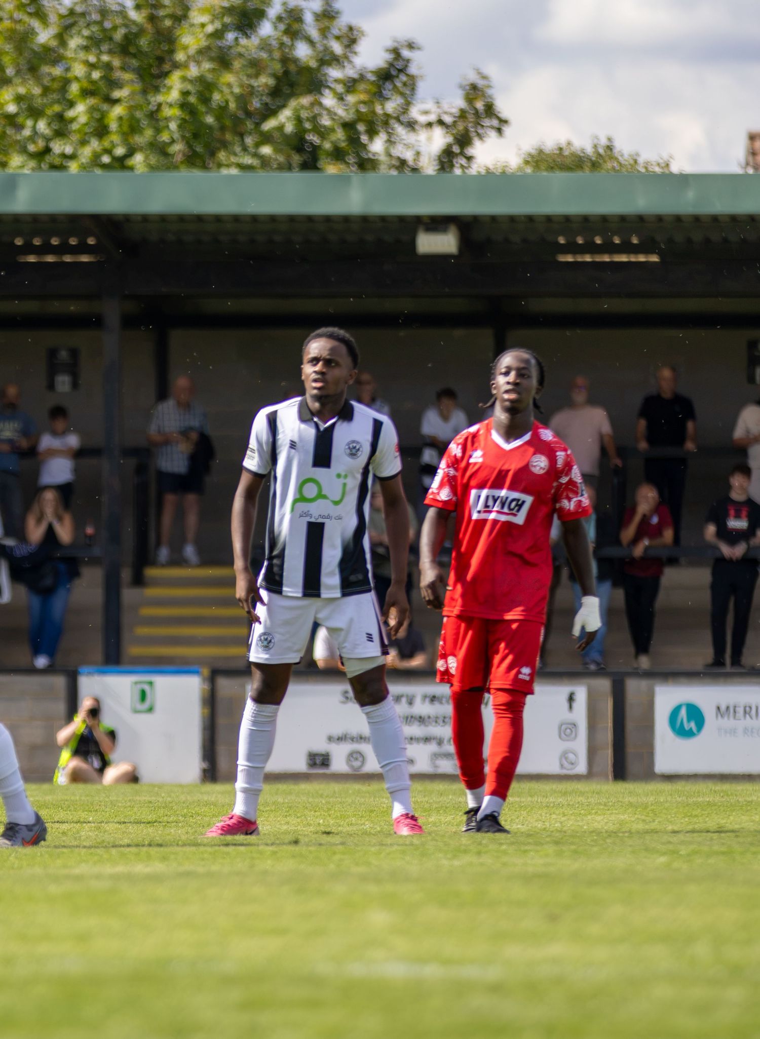 Two footballers in white and red kits stand side by side during break in play outdoors.
