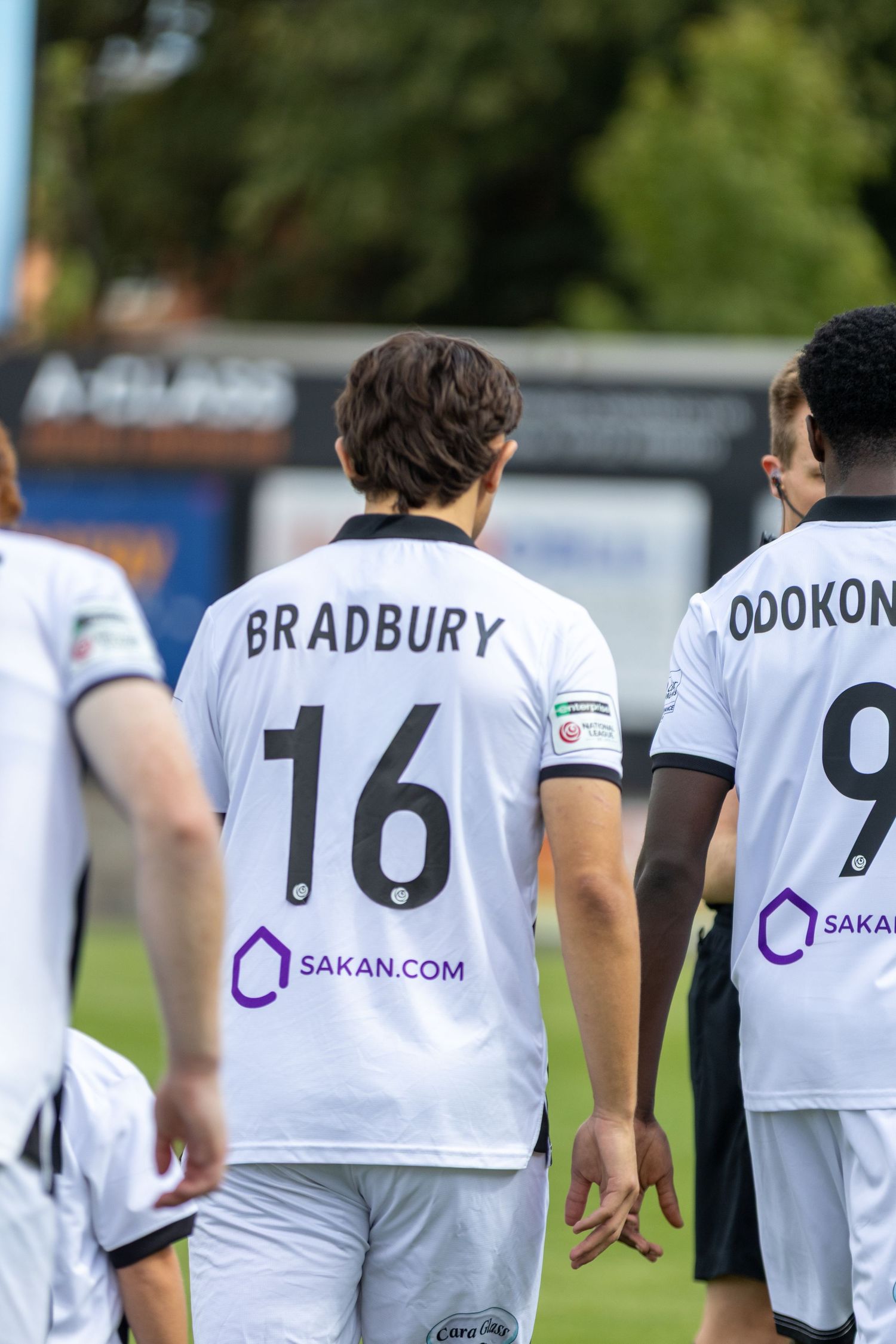 Bradbury number 16 and Odokonyero number 9 in white Sakan.com sponsored football shirts walking on pitch.