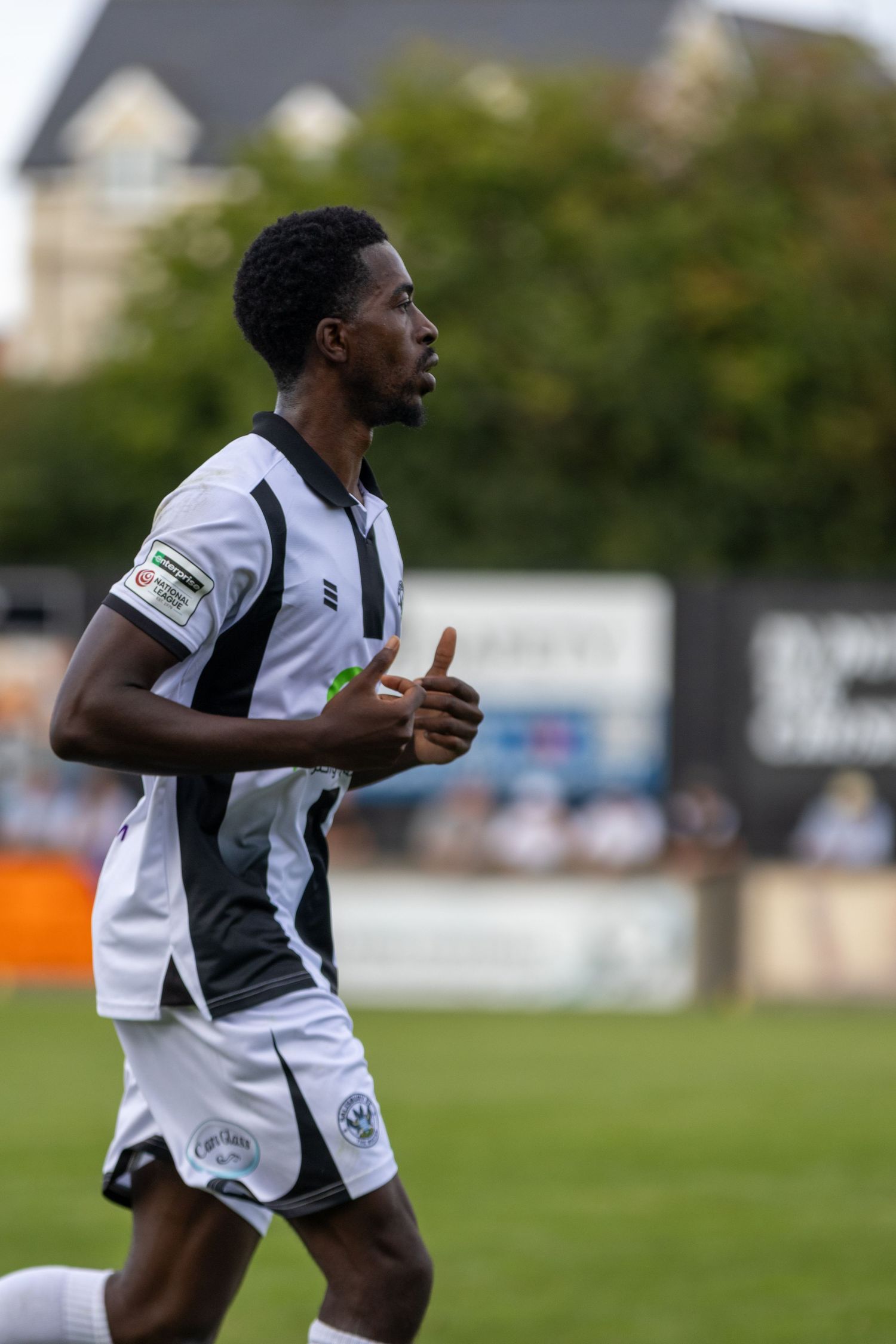 A male soccer player in a black and white striped kit jogging on a football pitch during a match.