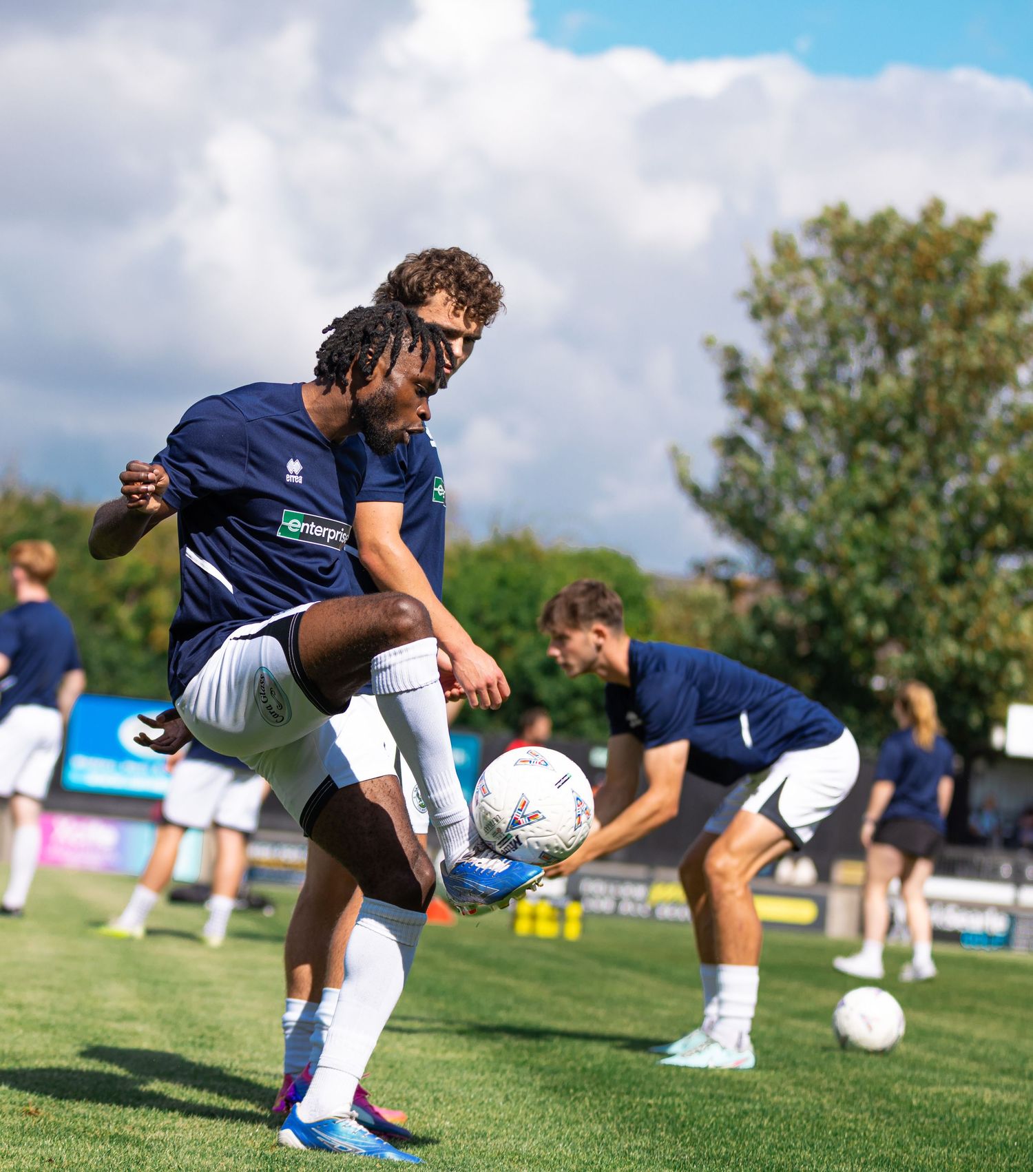 Soccer players in navy uniforms practice ball control drills on a green field during an outdoor training session.