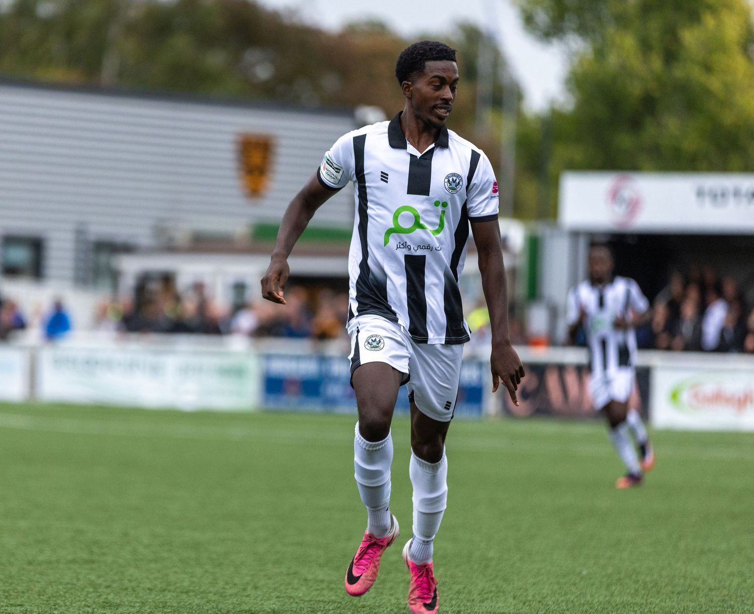 Football player in black and white striped kit sprinting on green pitch during a match.