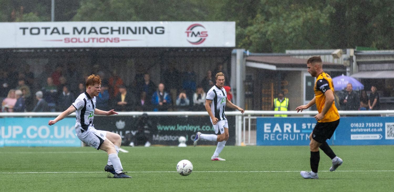 Two football players compete for the ball during a match, with advertising boards visible in the background.