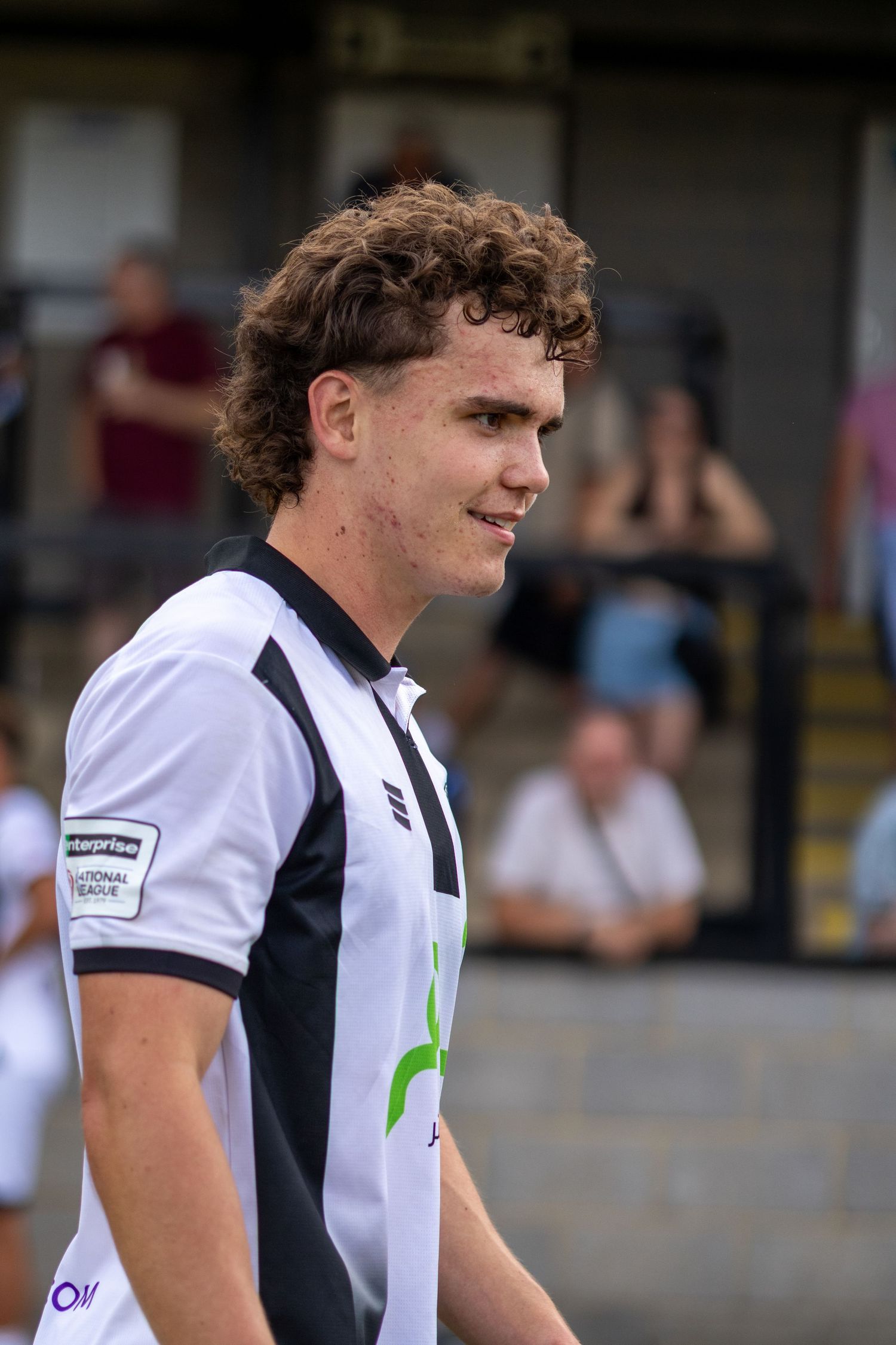 Young curly-haired footballer in black and white National League jersey smiles during a match.