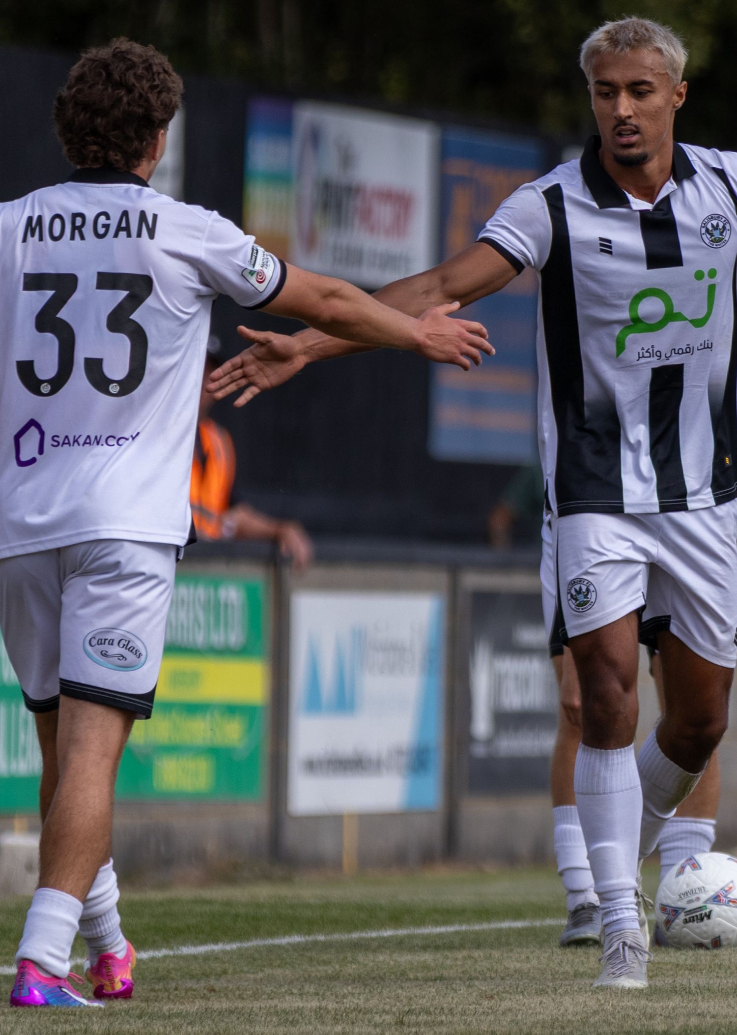 Two footballers in black and white jerseys celebrate, player Morgan number 33 high-fiving teammate.