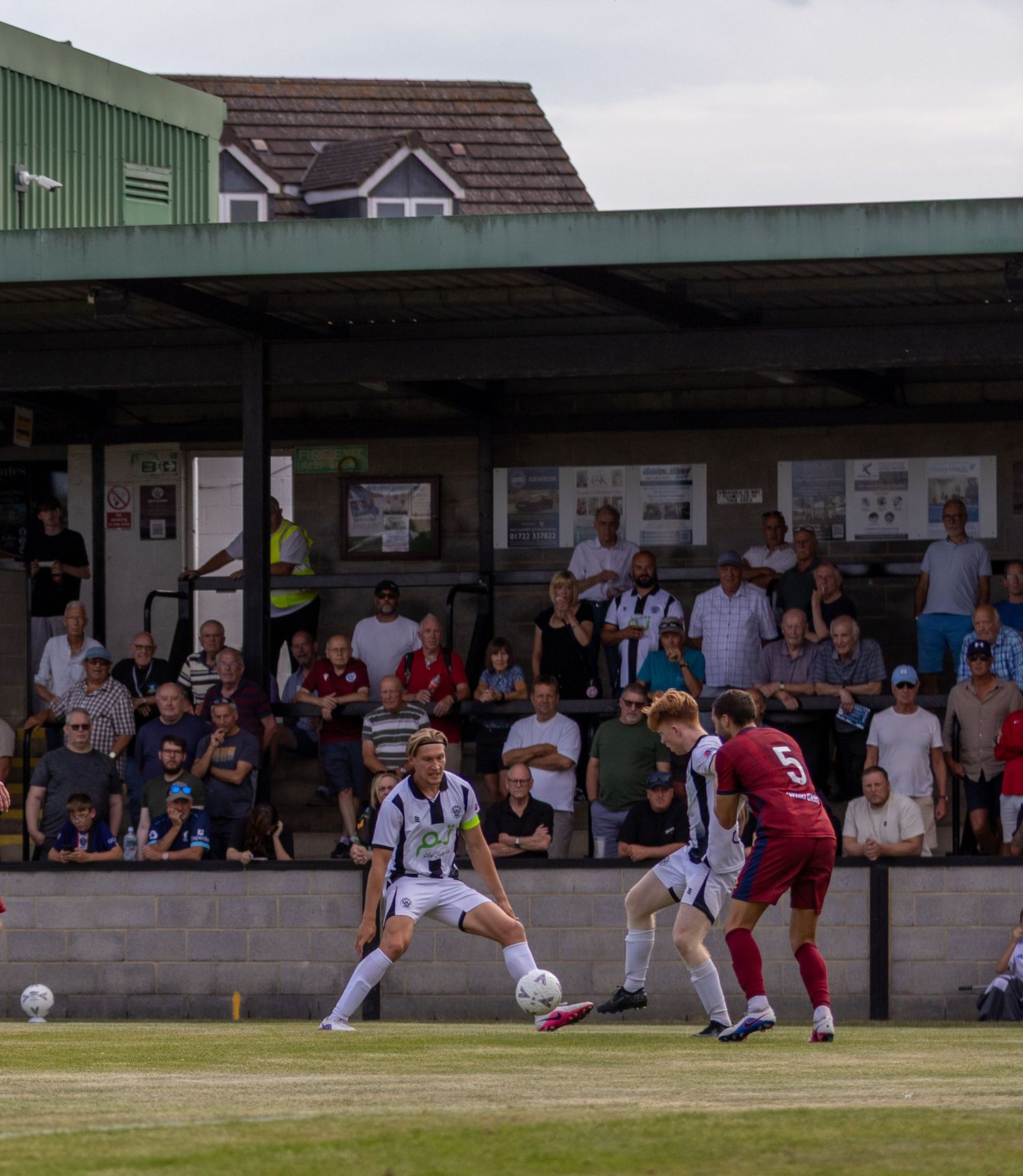 Two football players contest possession near the sideline with a crowd of spectators watching from the stands.