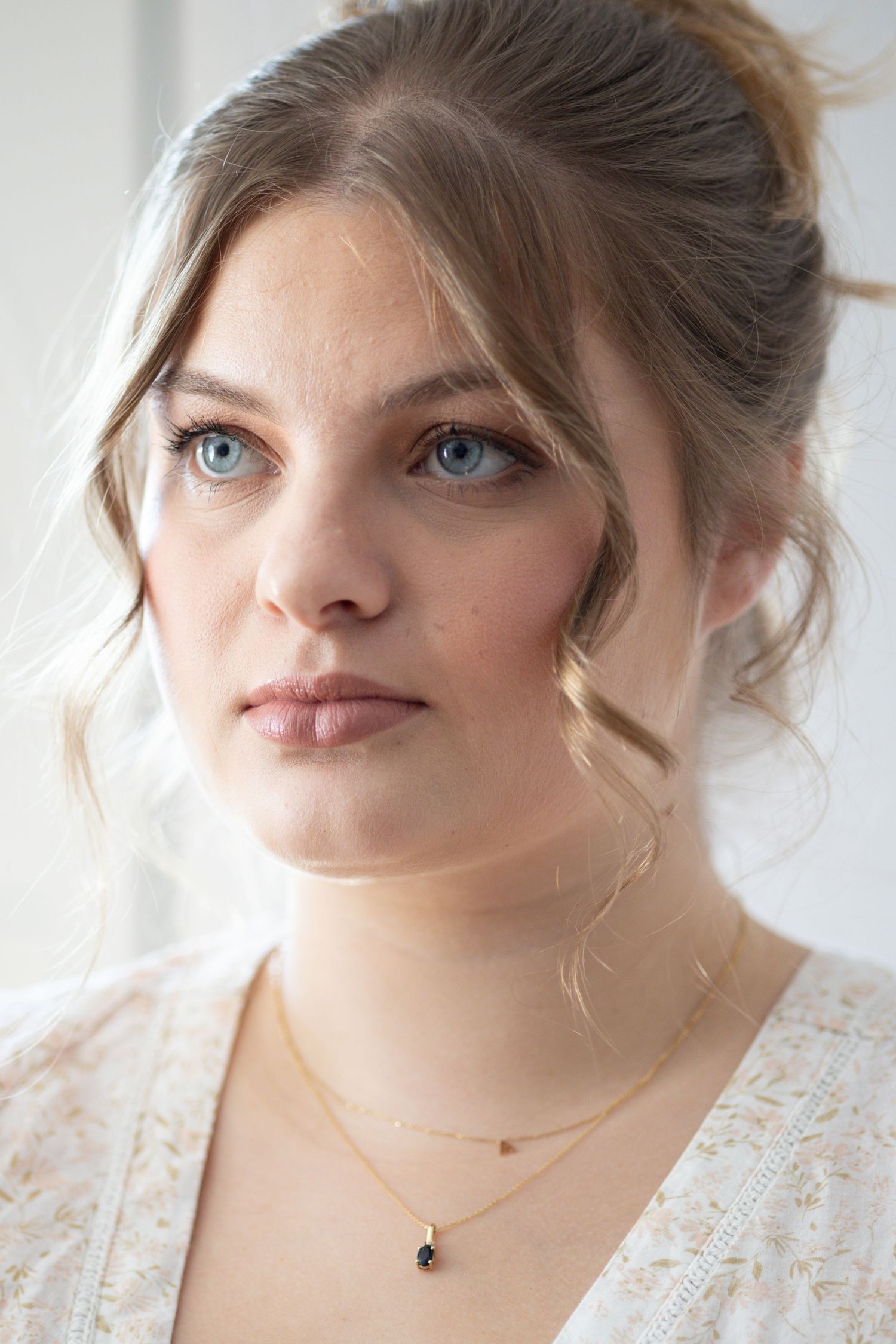 Close-up portrait of blue-eyed woman with elegant updo and gold pendant necklace.