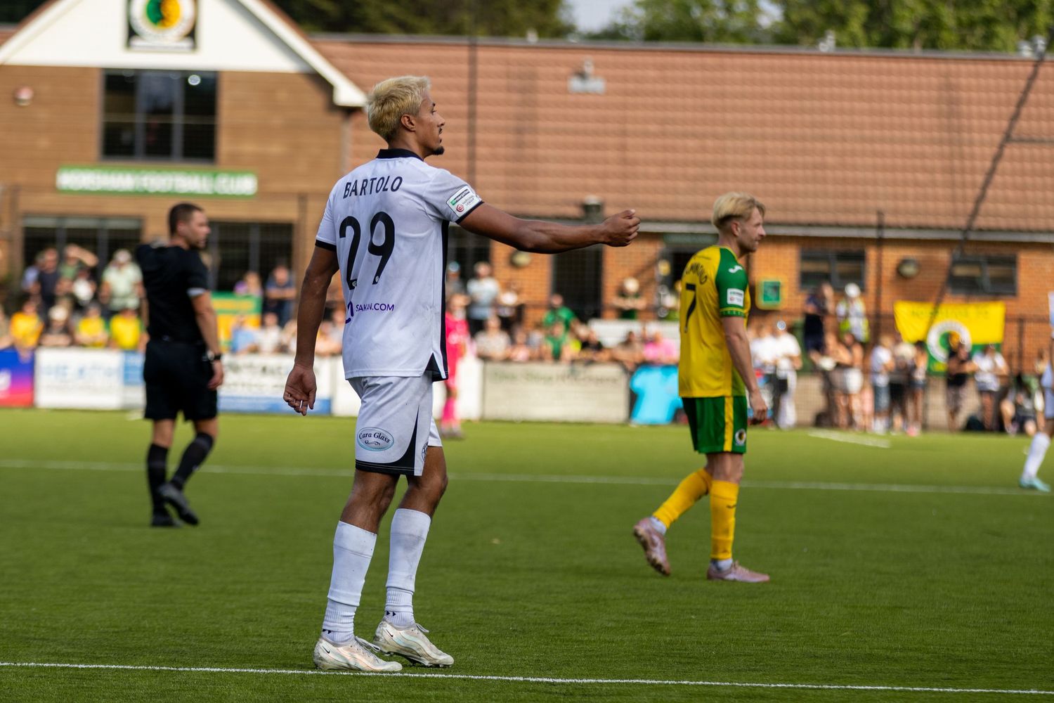 Player Bartolo number 29 in white kit gestures during a football match against a team in yellow and green.