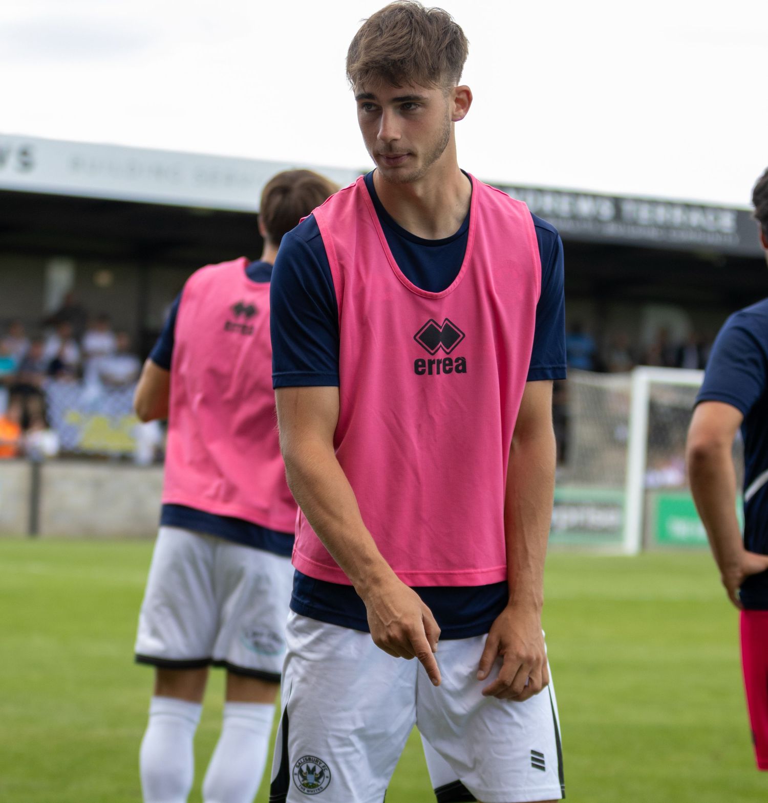 Young soccer player in pink training bib prepares during a football match warmup.