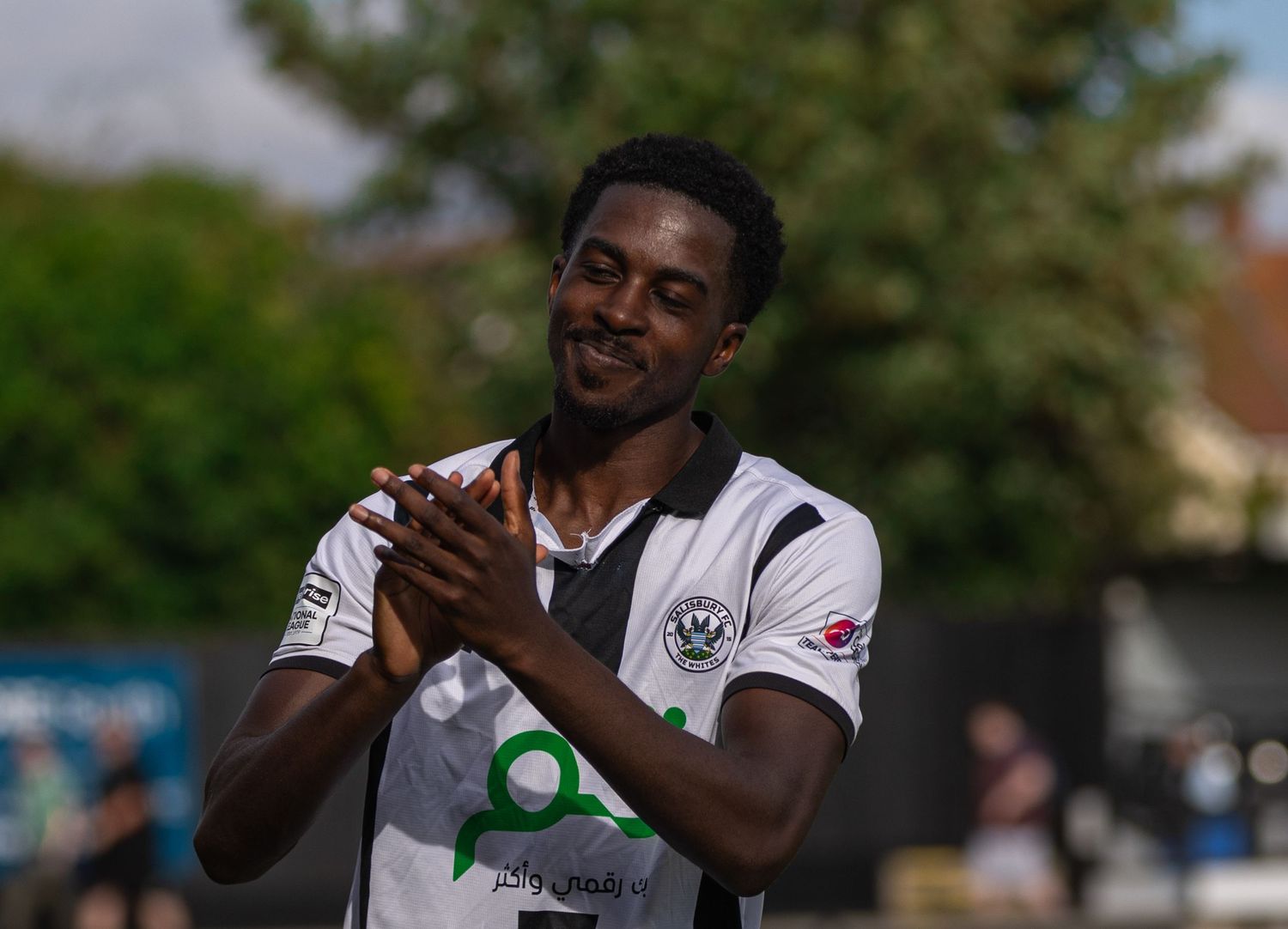 Football player in white and black kit clapping on a sunny matchday.