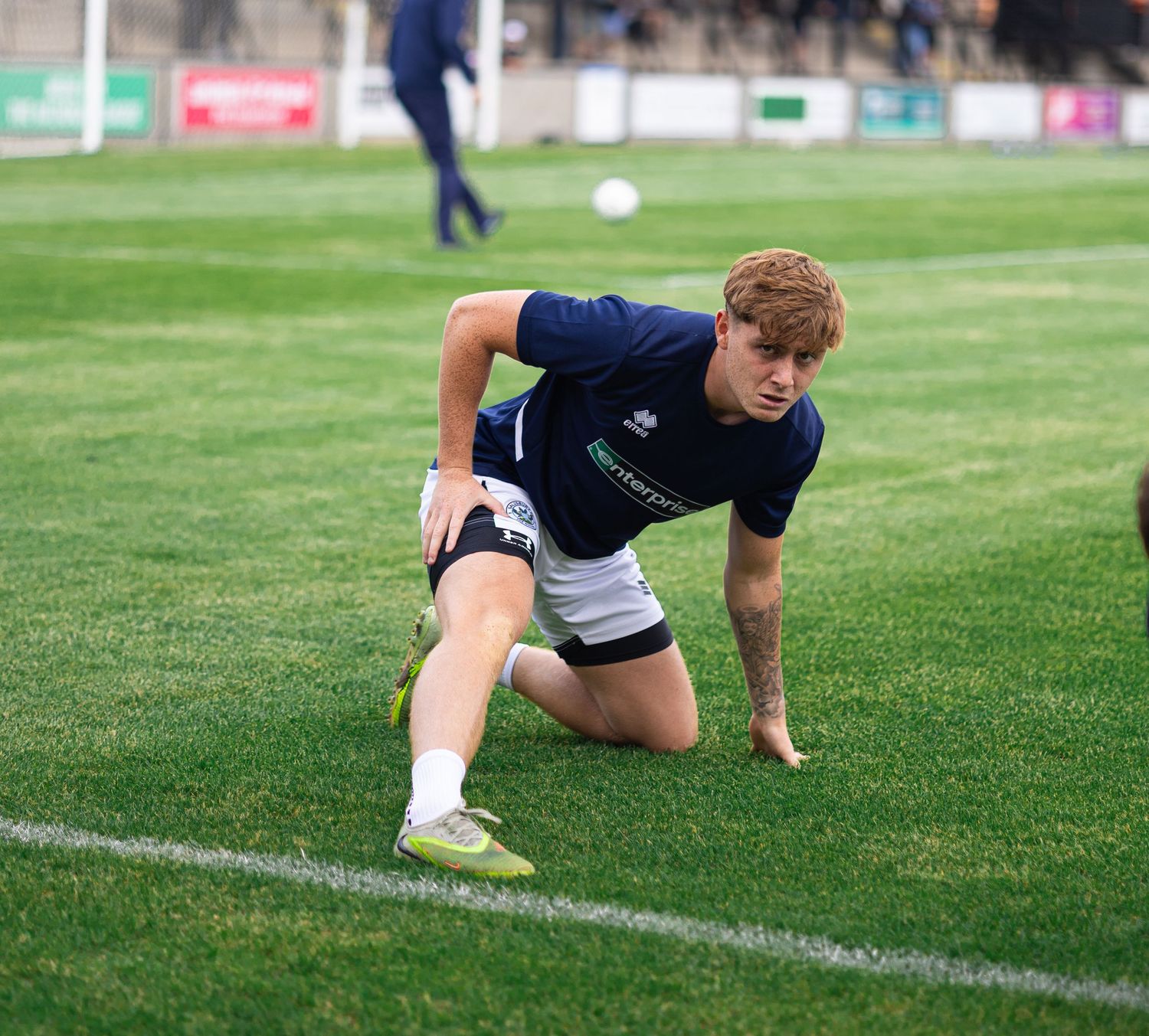Young rugby player in navy kit stretches on grass field during pre-match warm-up session.