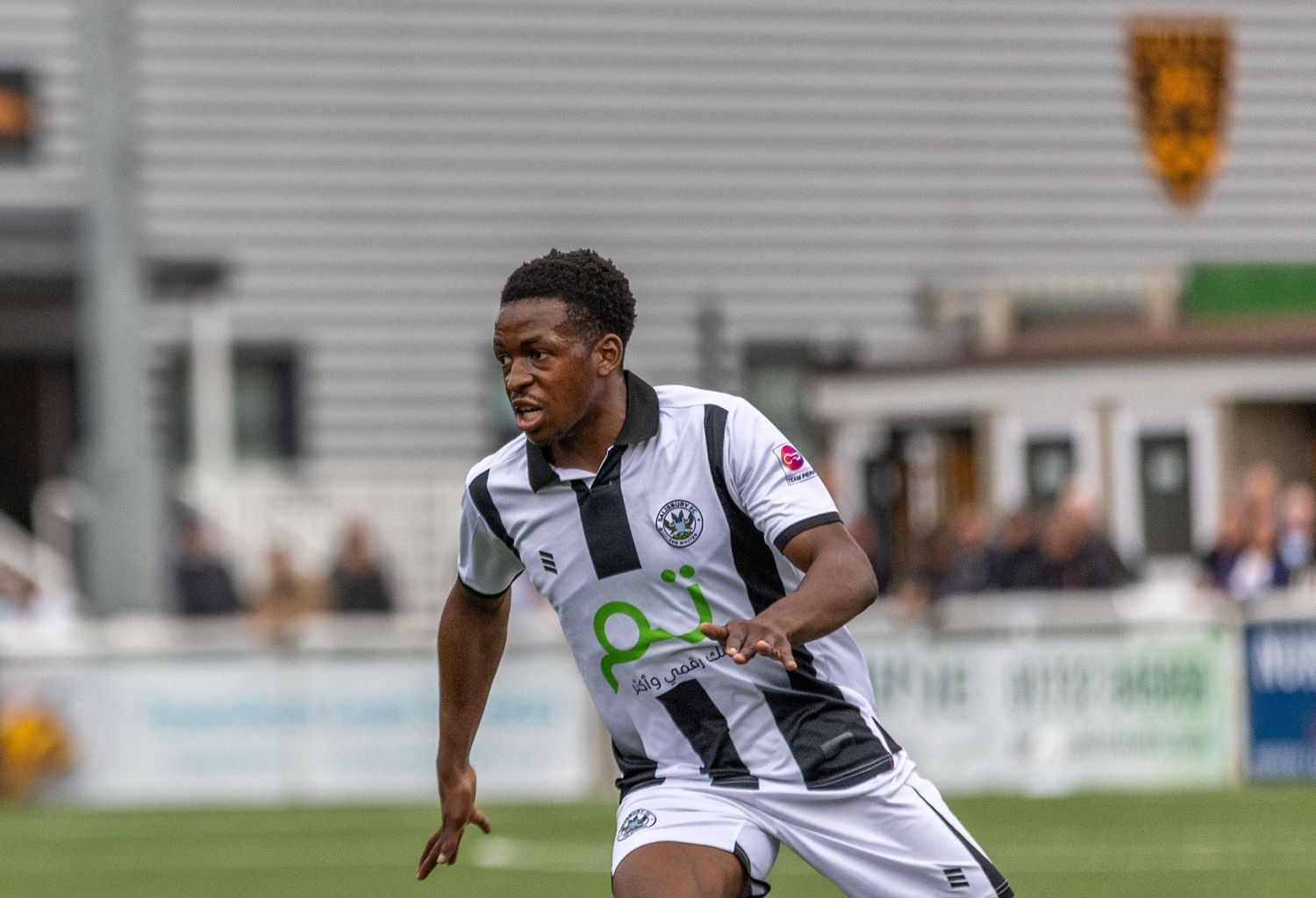 A young footballer in black and white kit dribbles during a match on a green pitch.