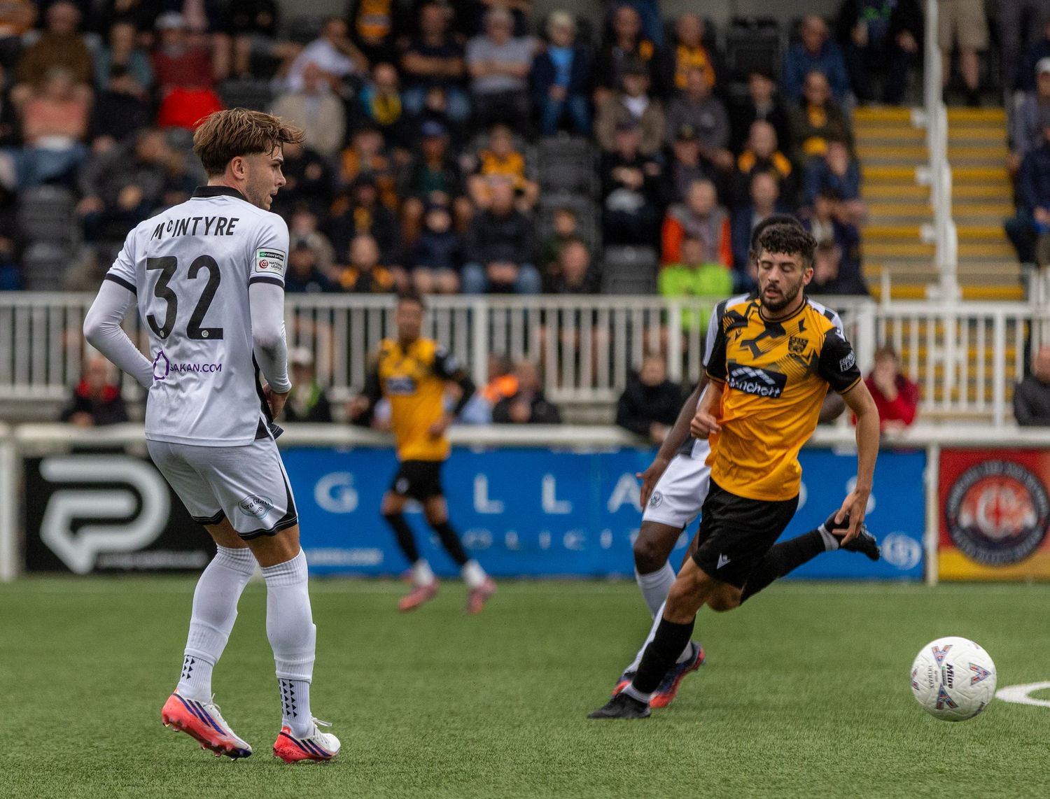 Two soccer players compete during a match, one wearing number 32 white kit, the other in black and yellow.