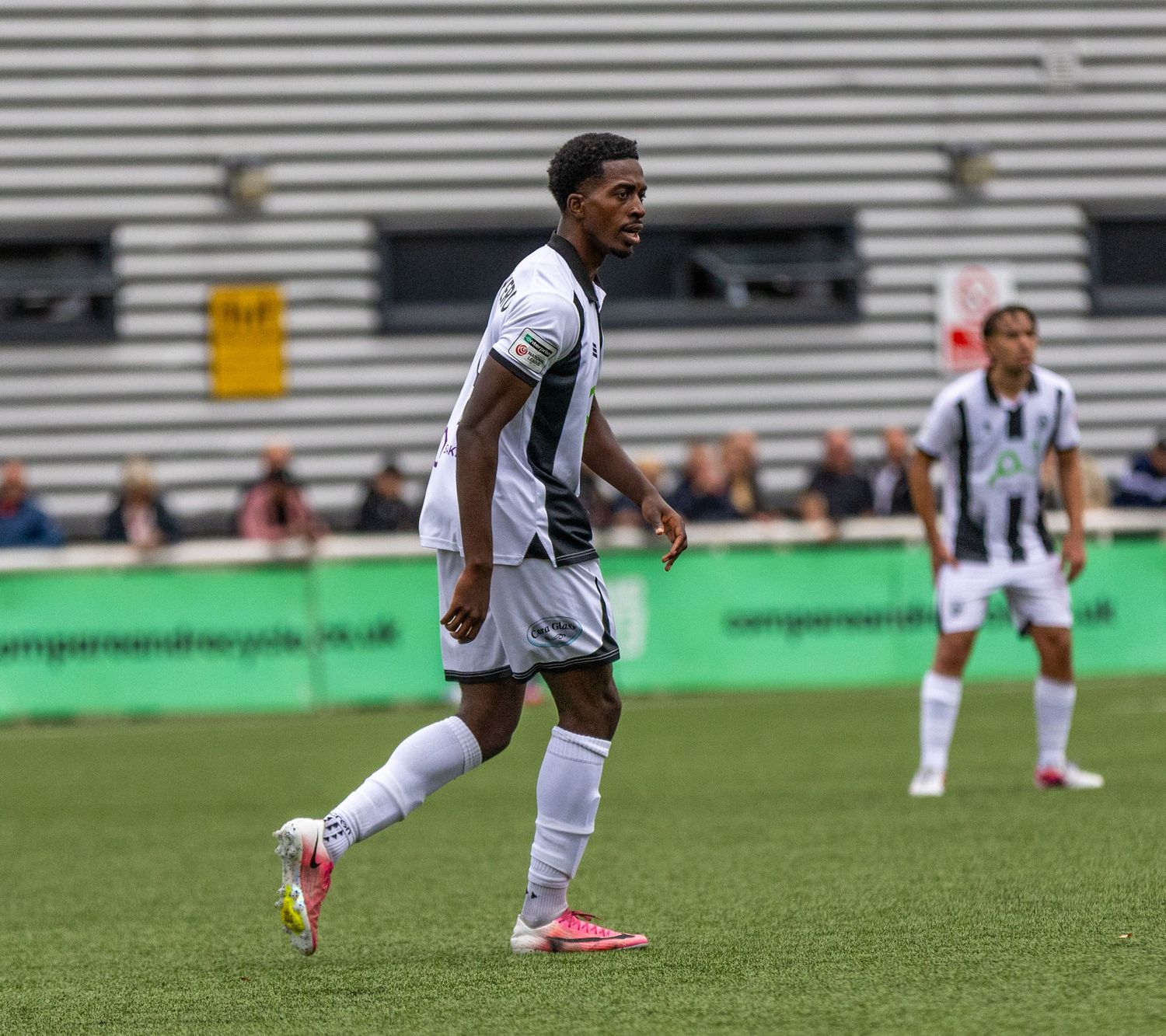 Soccer player in black and white striped kit jogging on green pitch during a match.