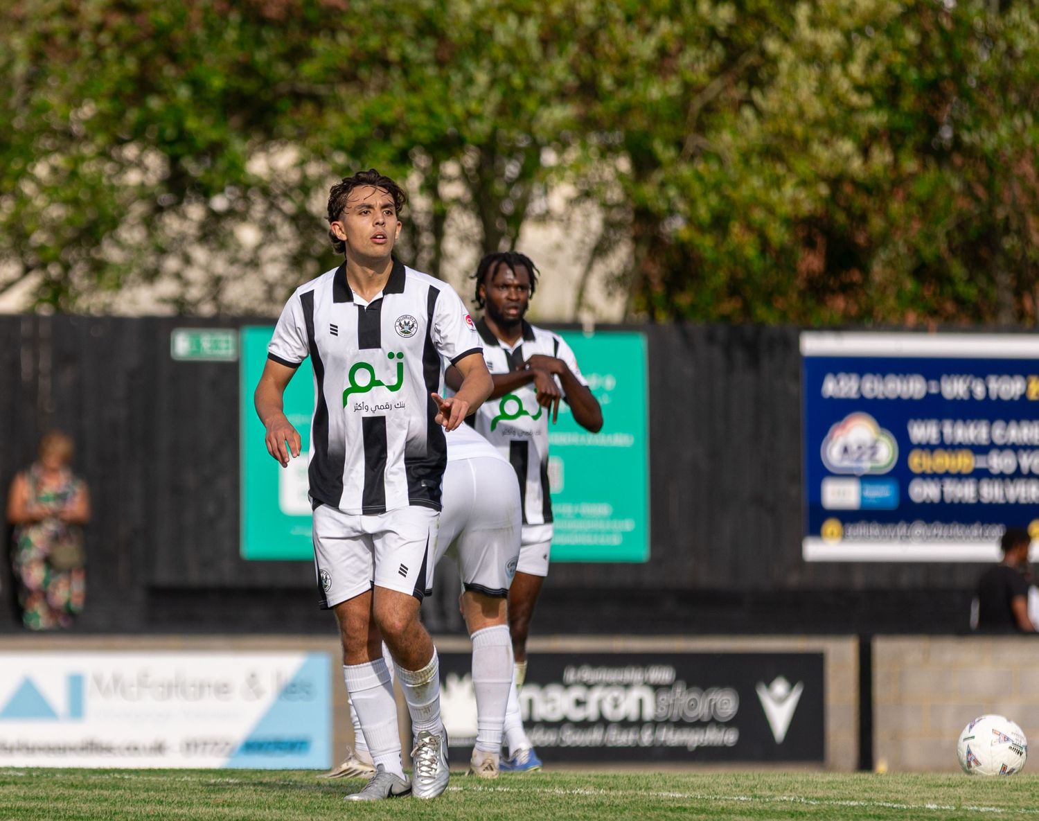Two soccer players in black and white uniforms compete on a green field during a sunny outdoor match.