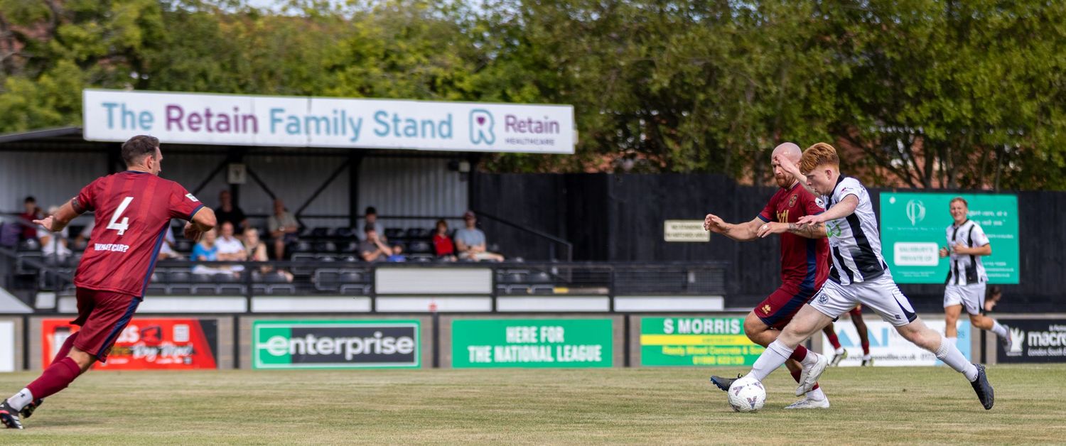Football players compete for the ball in front of the Retain Family Stand during a non-league match.