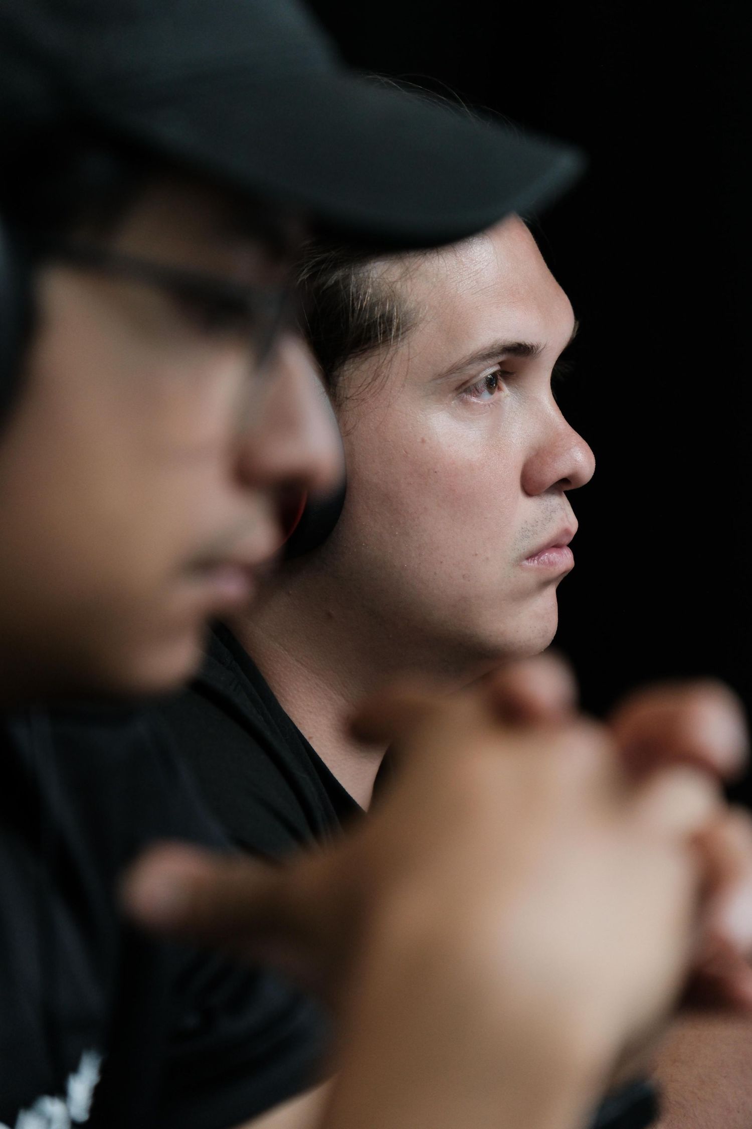 Two focused men in black caps sit together against dark background.