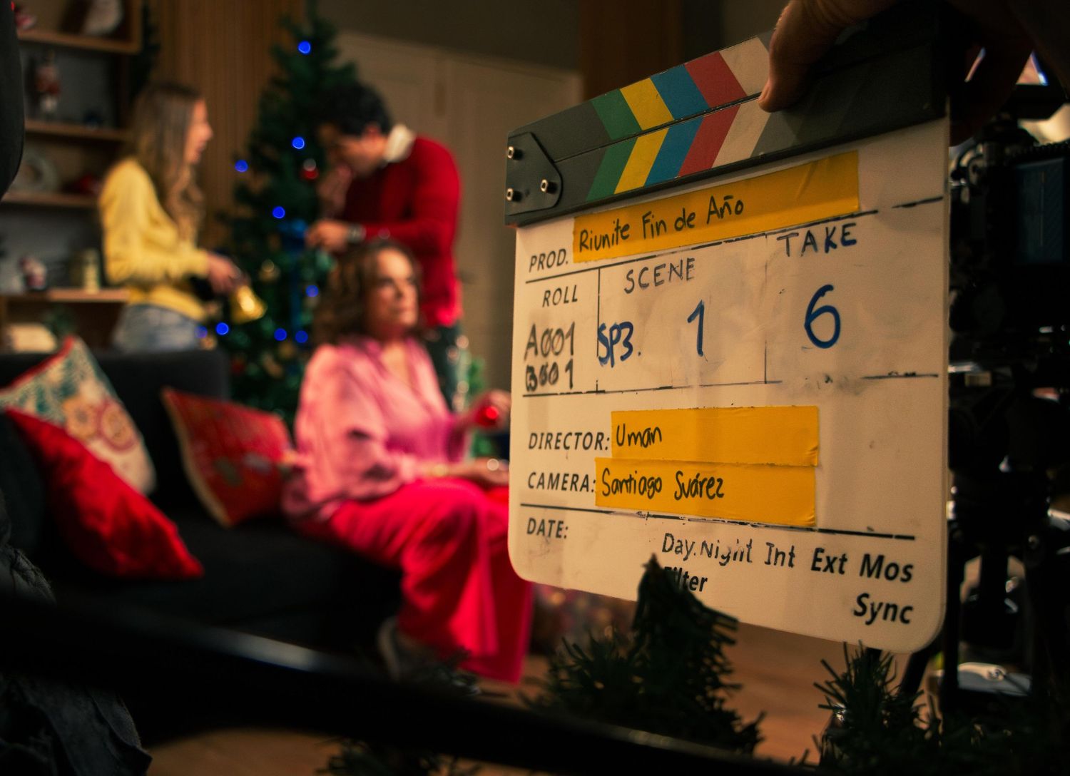 Close-up of a film clapperboard on a festive Christmas-themed movie set with actors in the background.