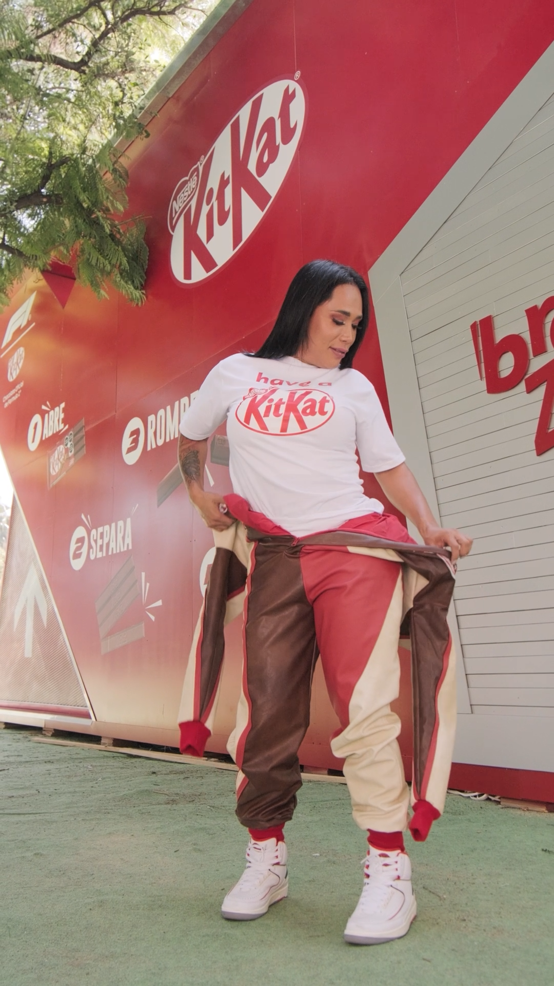 Woman wearing KitKat branded white t-shirt and brown pants poses in front of a red KitKat promotional display.