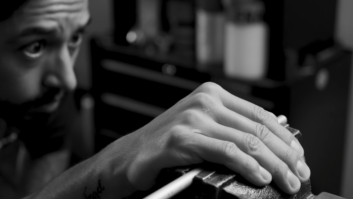 Black and white close-up of tattooed craftsman carefully working with hands on detailed project.