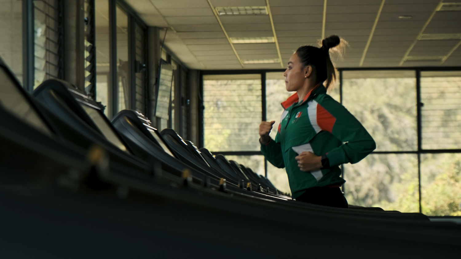 Female athlete in green and orange Mexico jacket running on a treadmill in a gym.