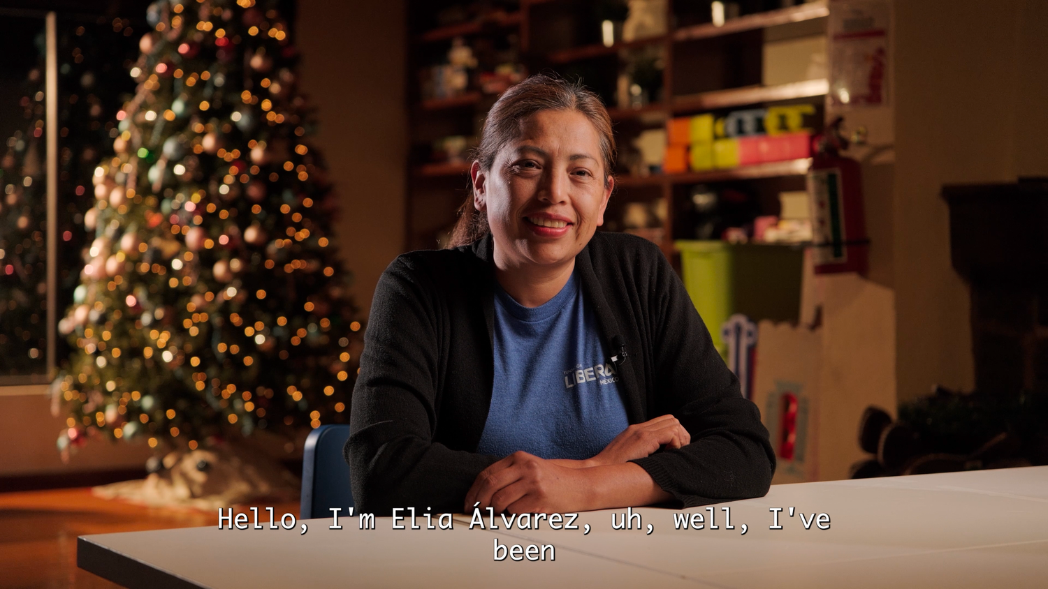 Woman with arms crossed smiling with subtitle text reading Hello, I'm Elio Alvarez and, well, I've been.