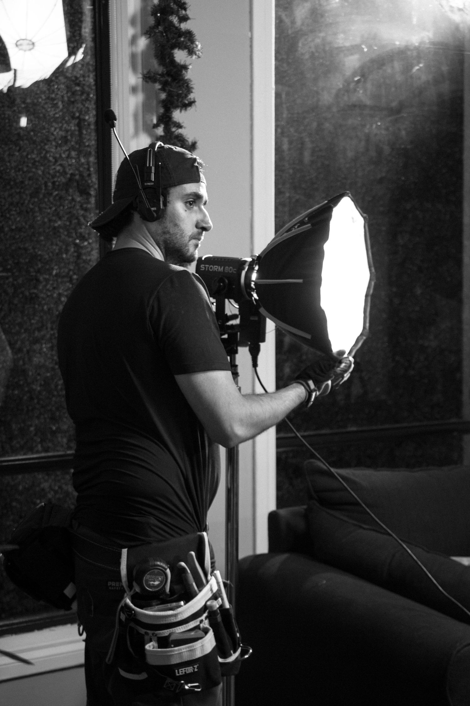 Black and white photo of a cameraman holding a softbox light modifier on a film production set.