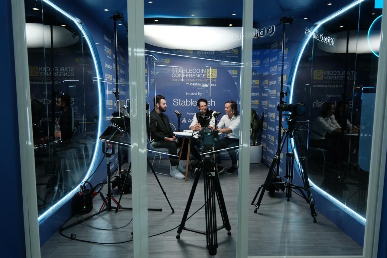 Three participants engage in a podcast recording inside a modern glass-walled studio booth at the Stabledash Conference.