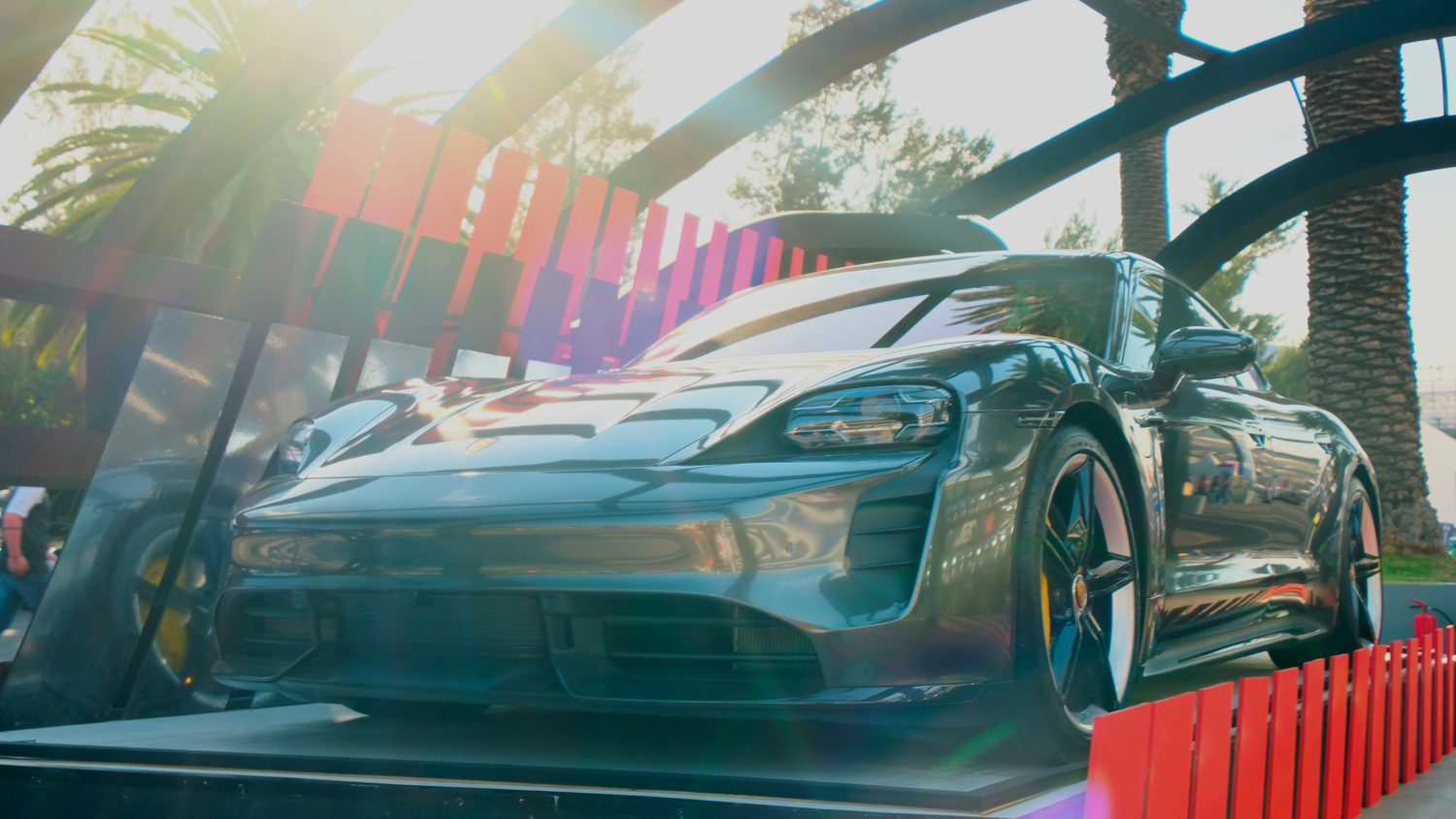Dark gray Porsche Taycan electric sports car displayed outdoors in bright sunlight.
