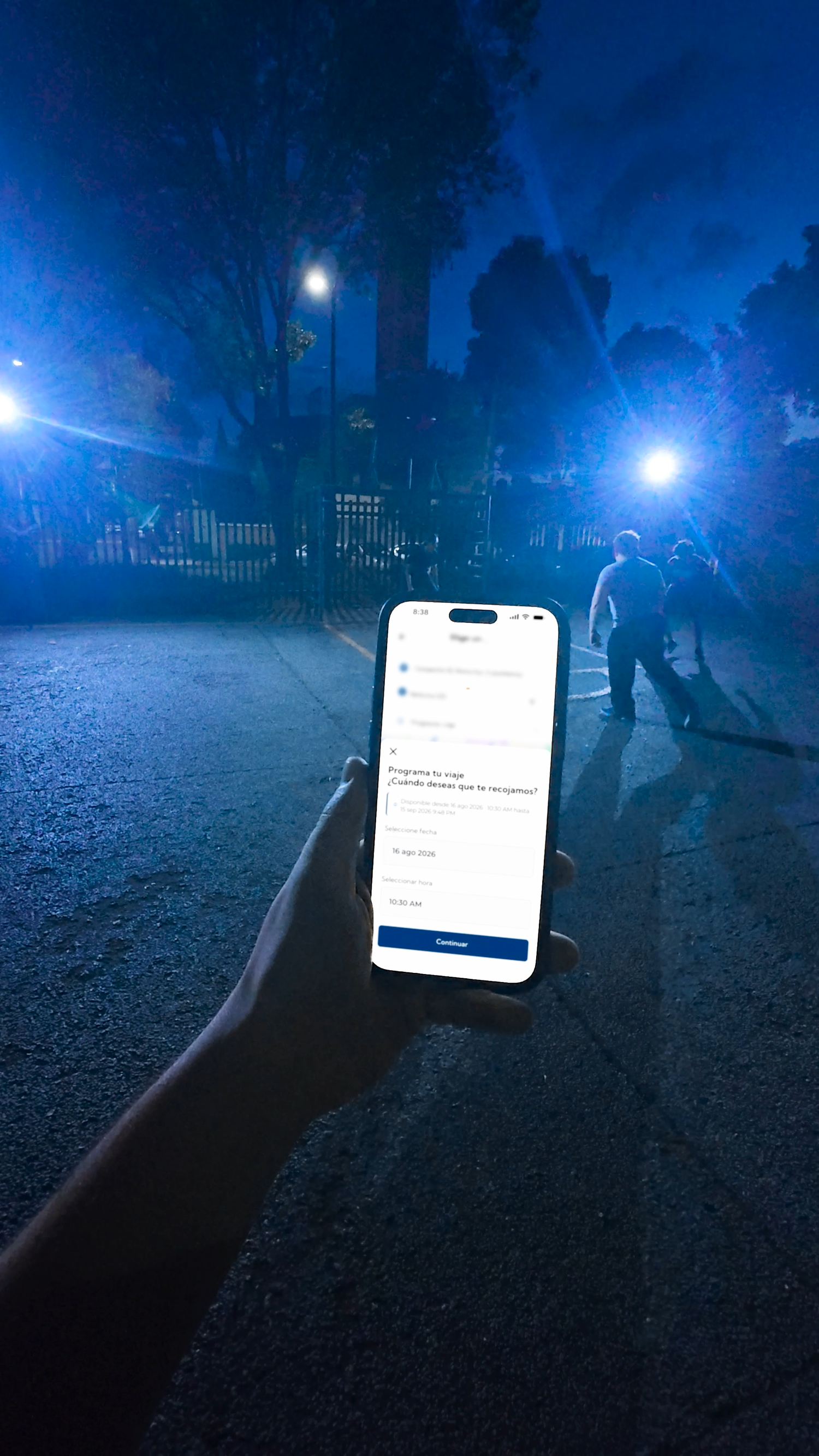 Hand holding smartphone with app open at night outdoors with blue lights in background.