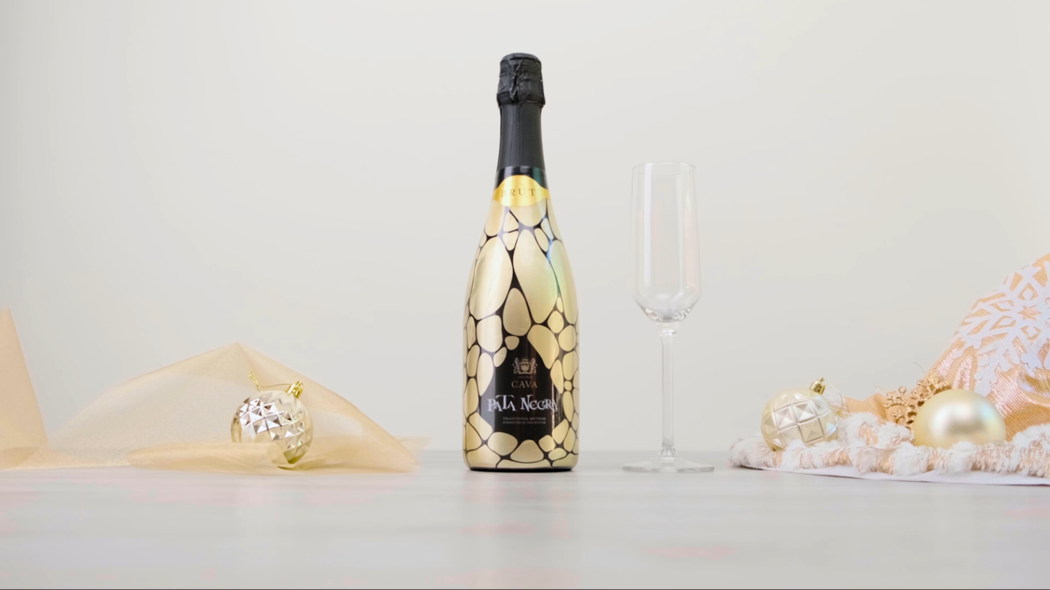 Elegant gold patterned Cava sparkling wine bottle beside a champagne flute with festive holiday decorations.