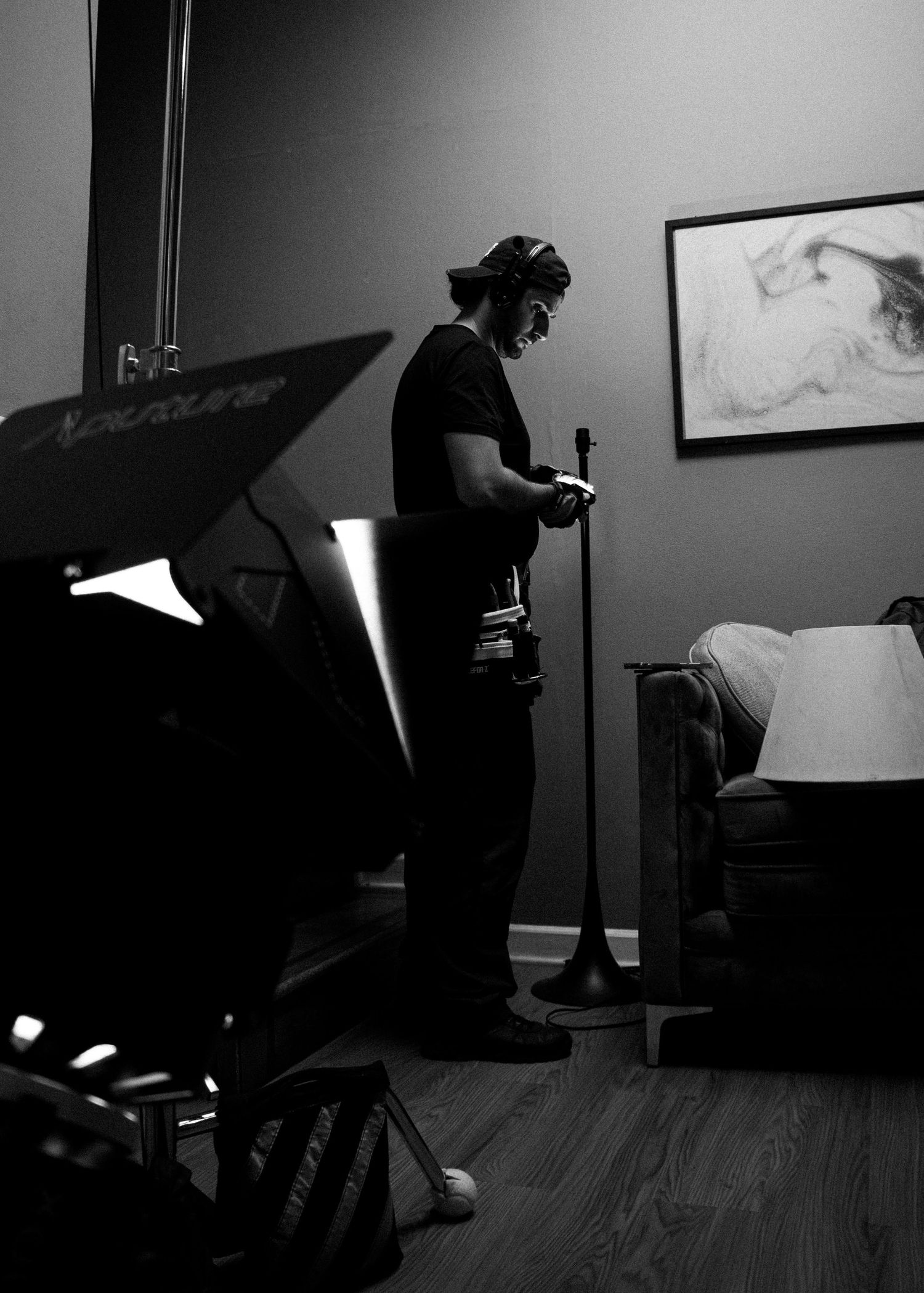 Silhouetted film crew member adjusts equipment in a dimly lit bedroom on a movie set.