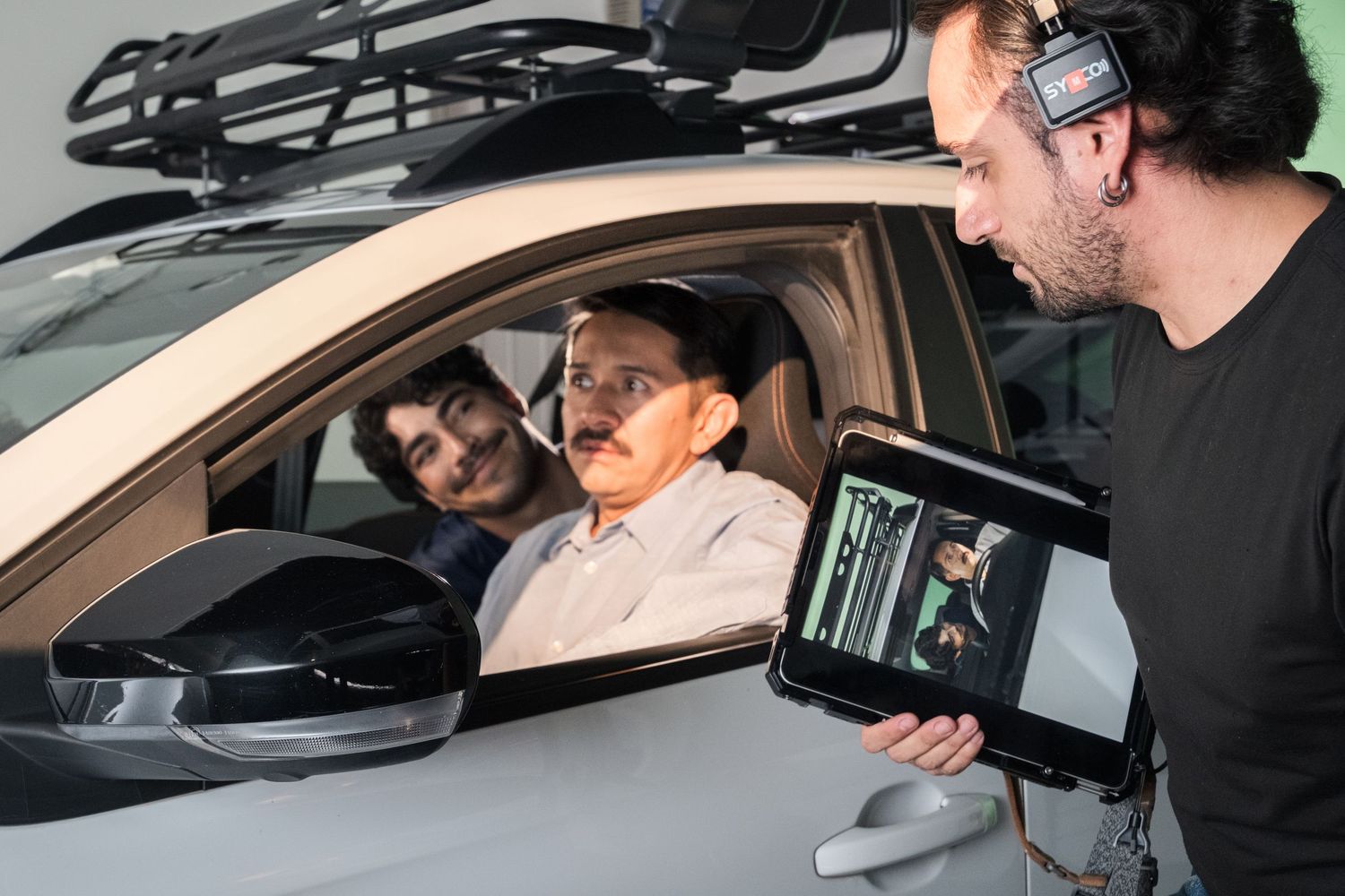 Film director showing tablet monitor to actors sitting inside a car on set.