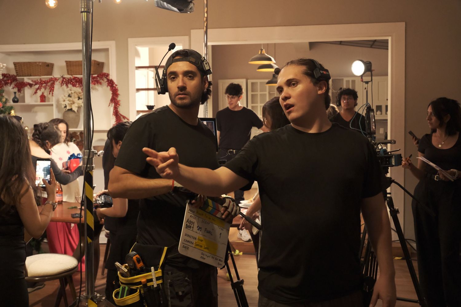 Two male crew members discussing shot composition on a busy film production set indoors.