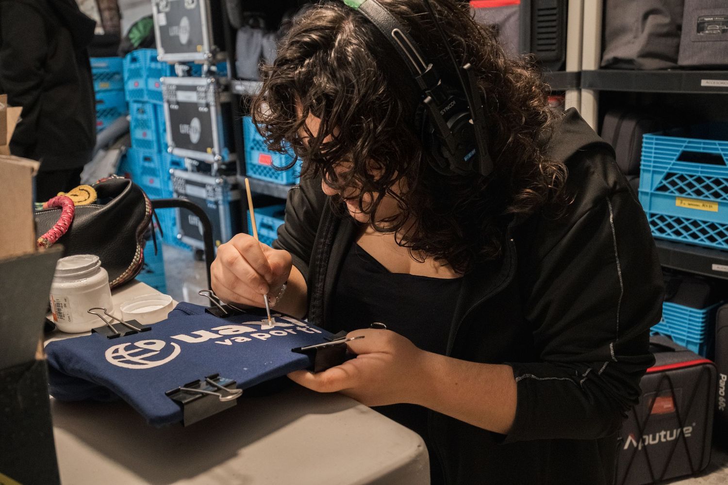 Female crew member signs merchandise at busy film production base camp.