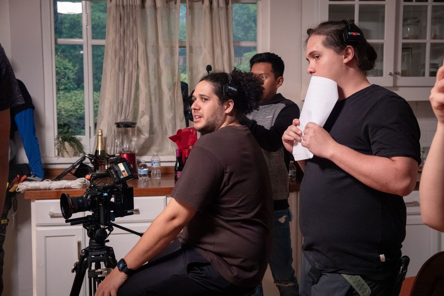 Film crew members reviewing a scene near a camera on a tripod during an indoor video production.