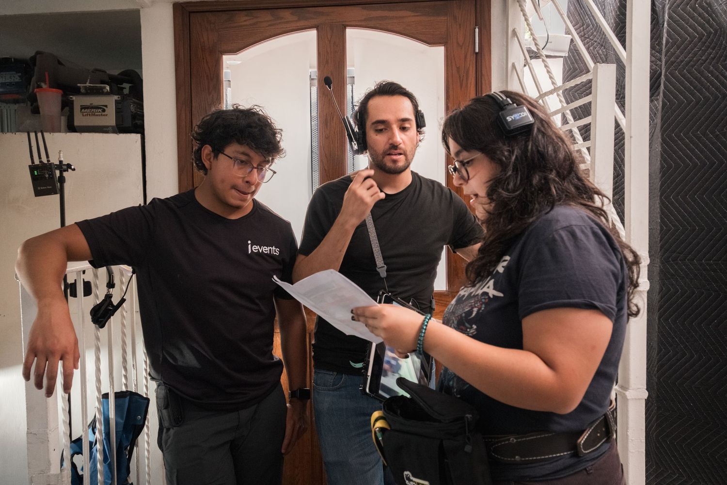 Three film crew members review a script together on a movie set indoors.