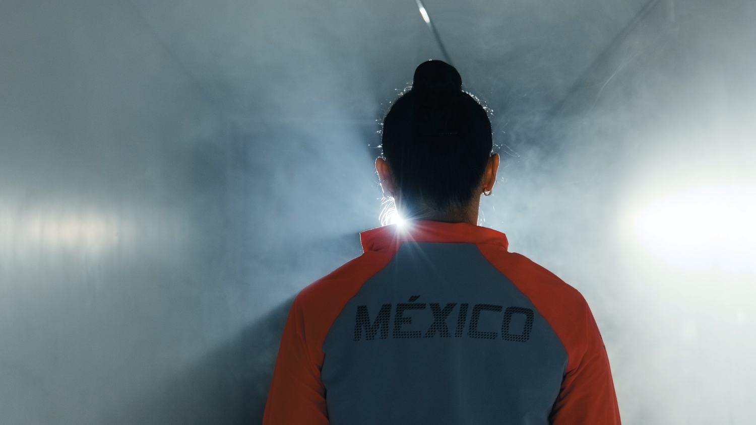 Athlete wearing Mexico jacket walking through a smoky tunnel toward a bright light.