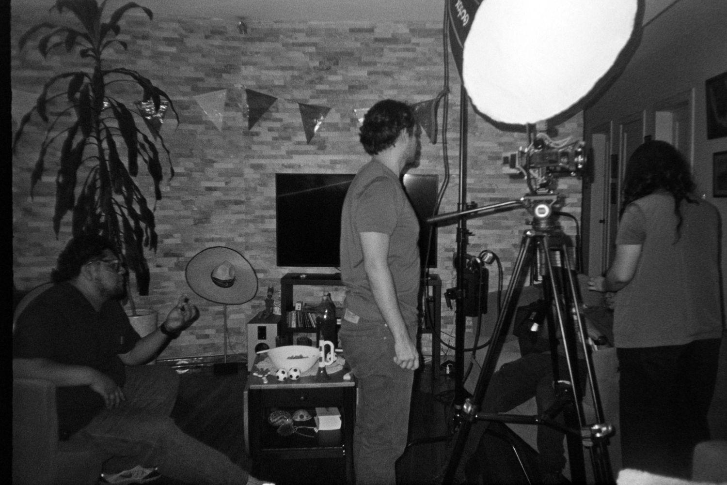 Film crew sets up lighting and camera equipment in a living room during an indoor shoot.