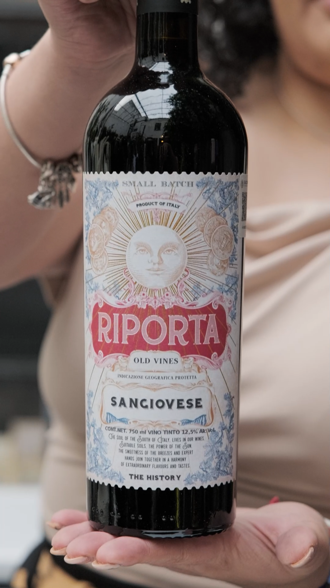 Woman holding Riporta Old Vines Sangiovese Italian red wine bottle with decorative sun label.