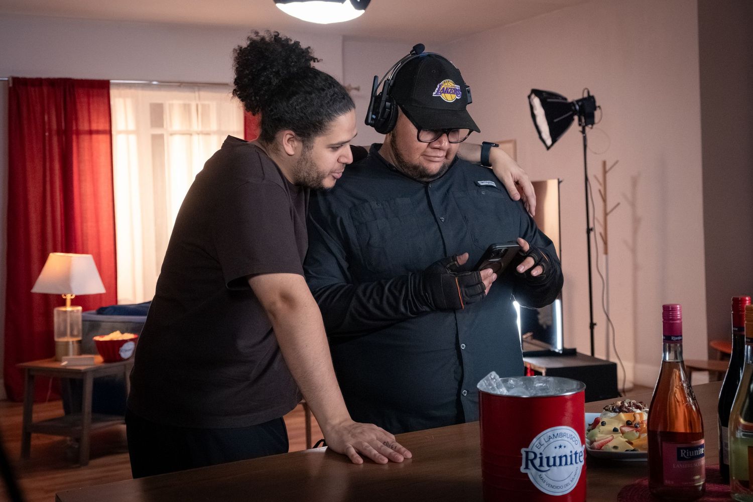 Two crew members review camera footage near Riunite wine on film set.