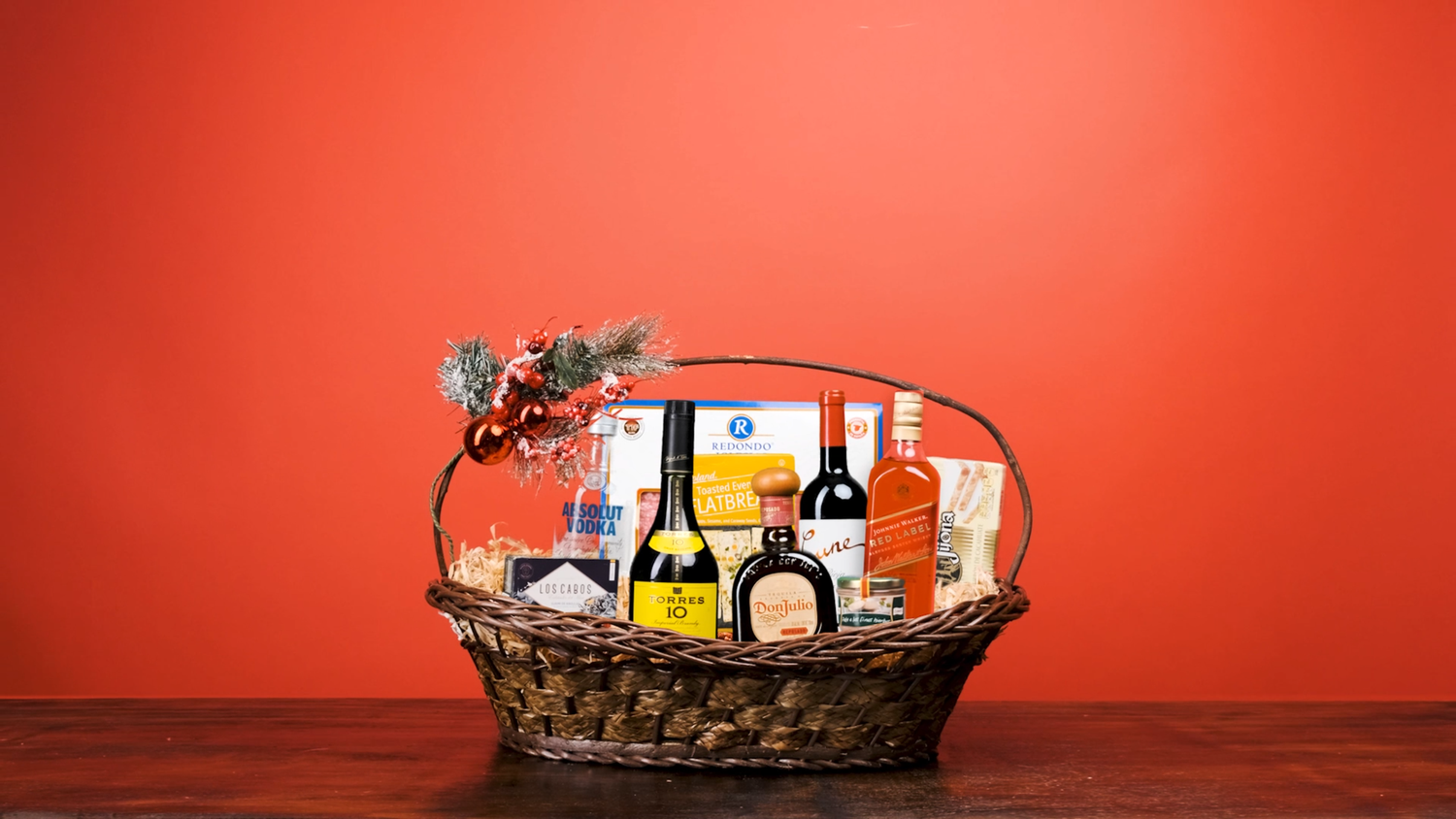 Festive gift basket filled with wines, spirits, and gourmet foods on a red background.