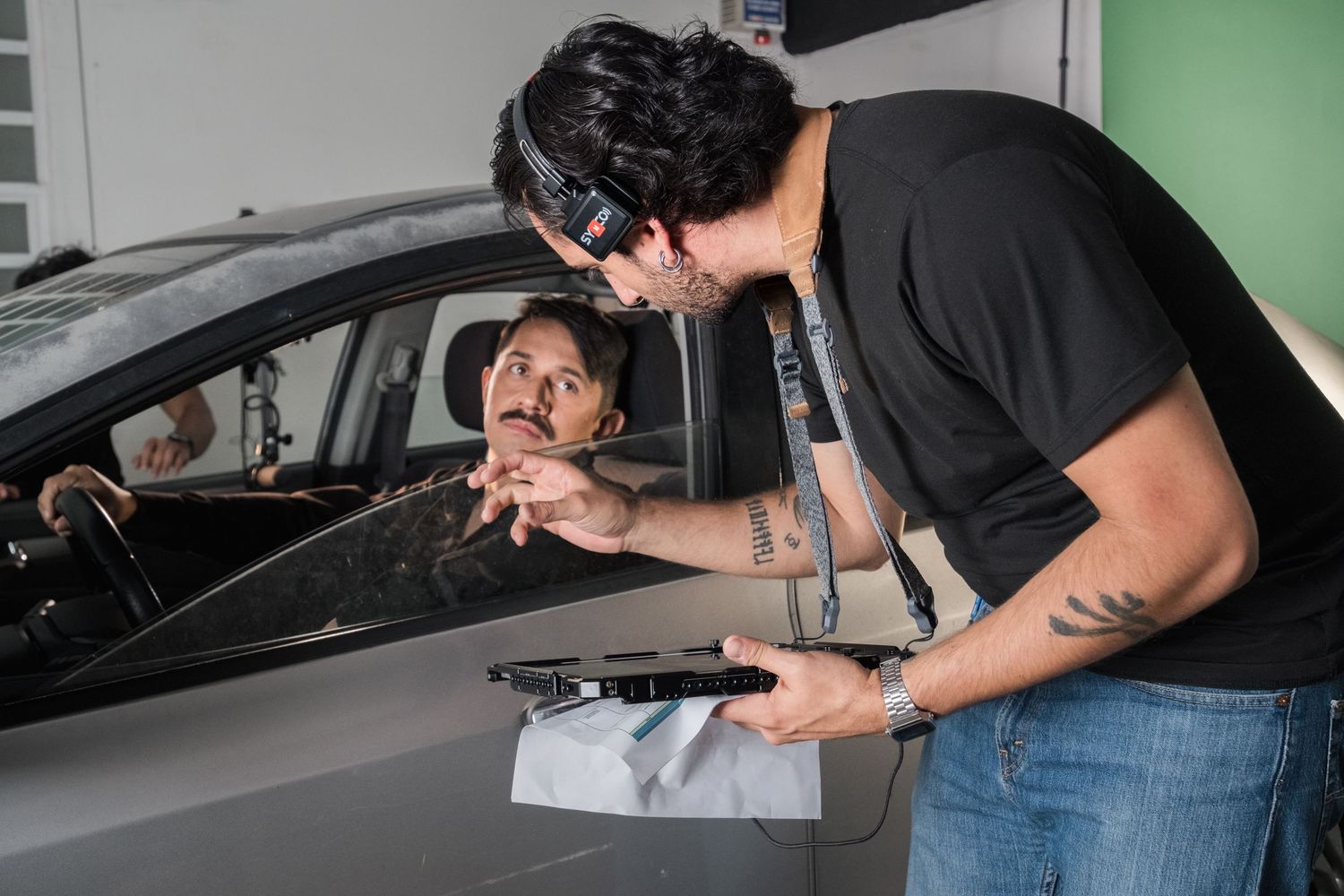 Film director reviews a shot on a monitor with an actor seated inside a car on set.