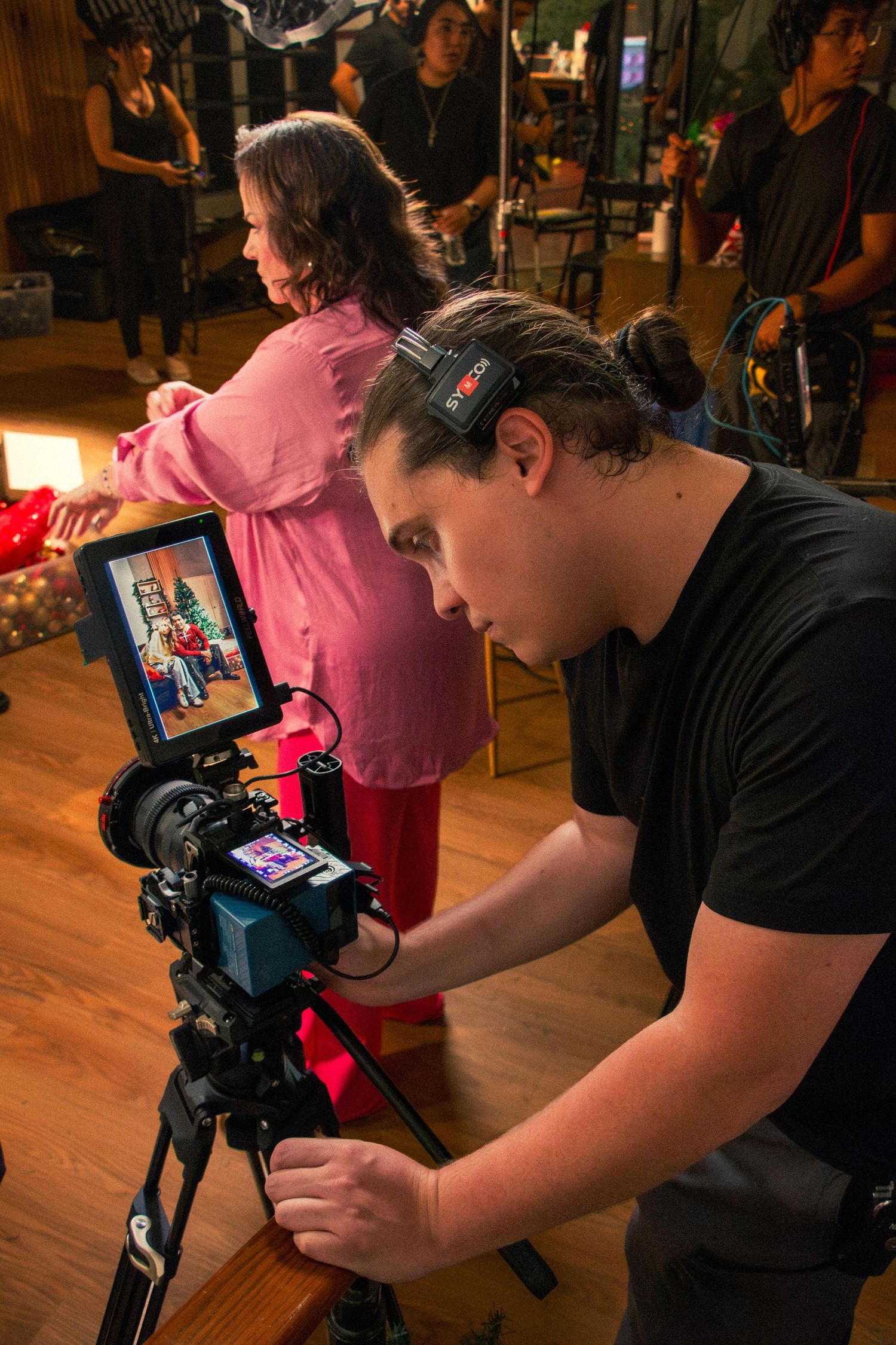 Behind-the-scenes photo of a cameraman reviewing a shot on a monitor during a colorful indoor film production.