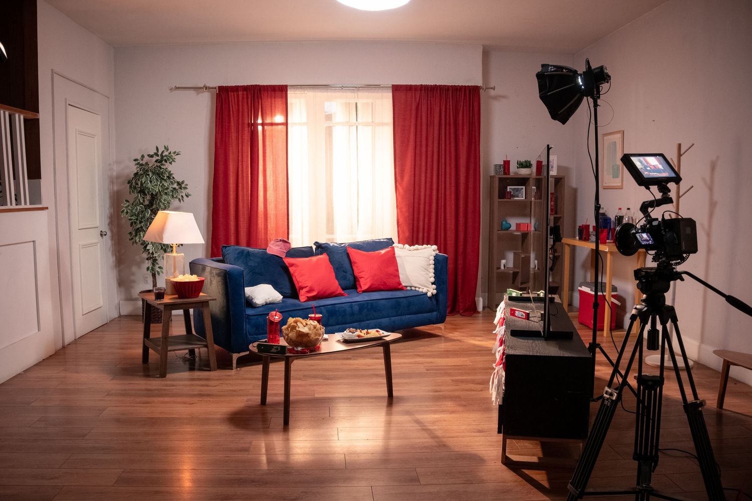 Professional film set featuring a blue sofa, red curtains, and camera equipment on tripod.
