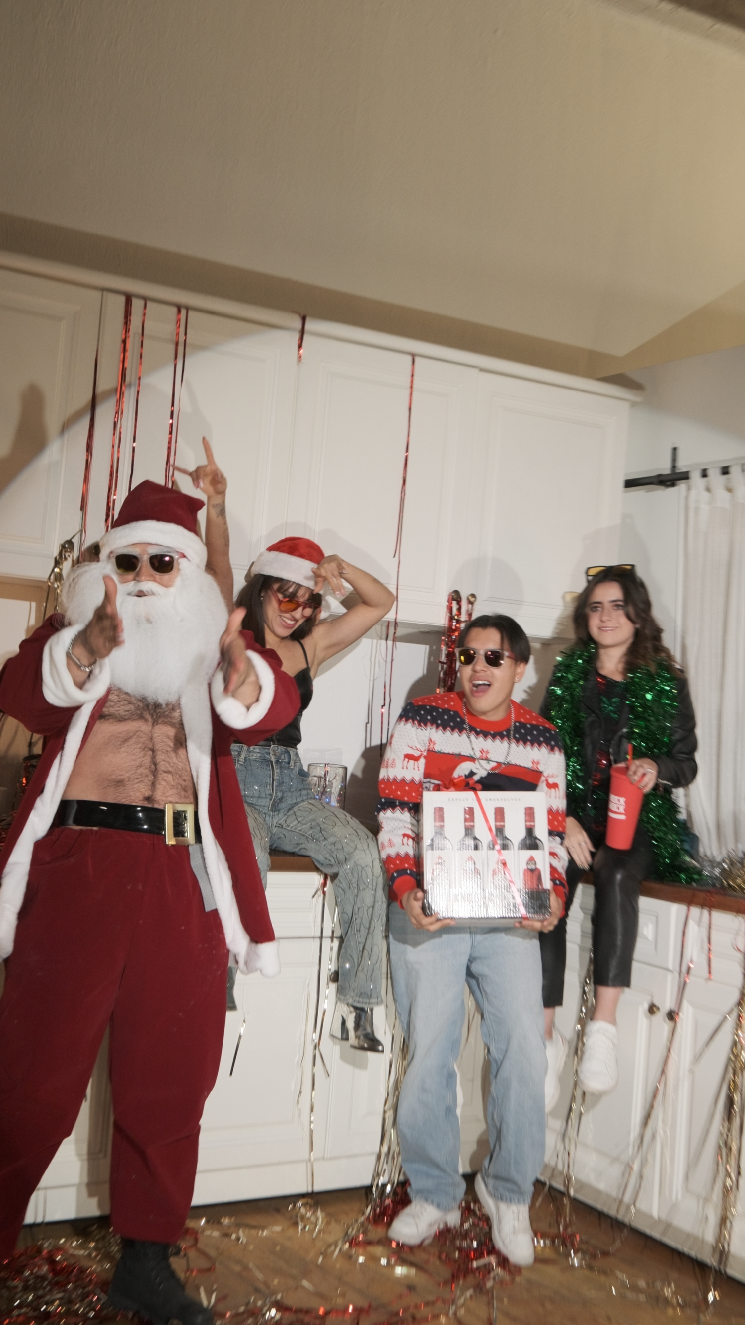 Group of four friends posing with Santa Claus holding Knock Knock wine gift box at Christmas party.