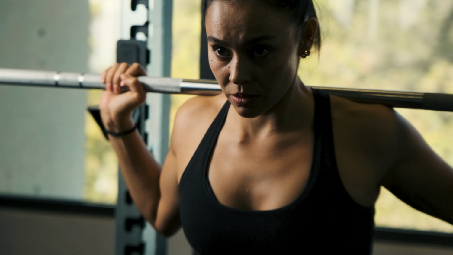 Focused woman in black sports bra performing barbell squat exercise in gym.